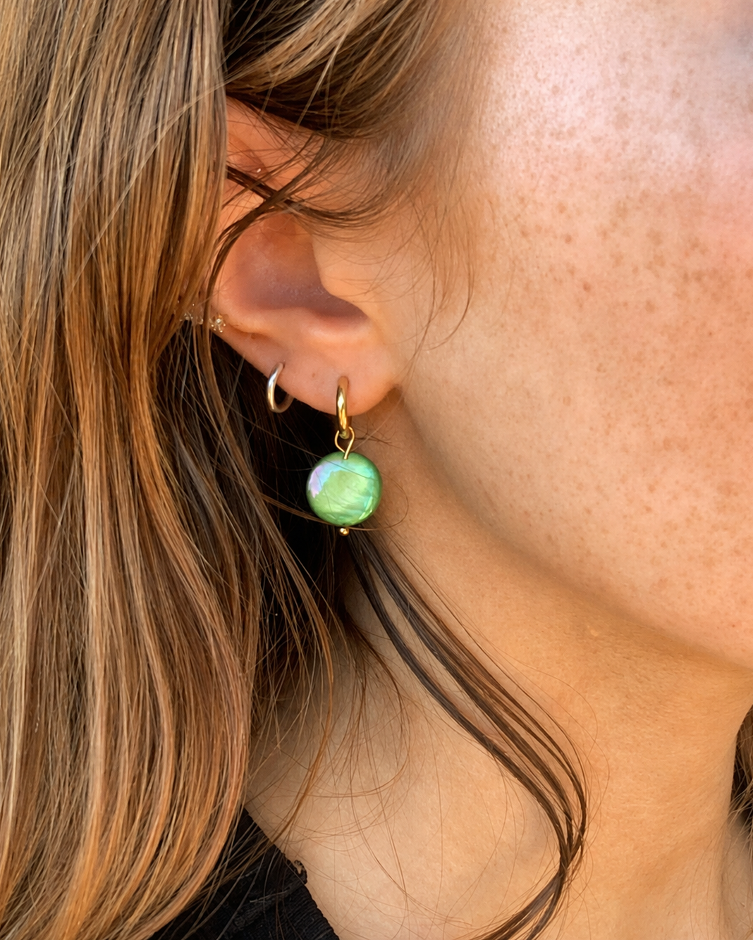 Close-up of a person wearing a gold earring with a green gemstone.