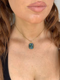 Close-up of a person wearing a gold necklace with a colorful pendant.
