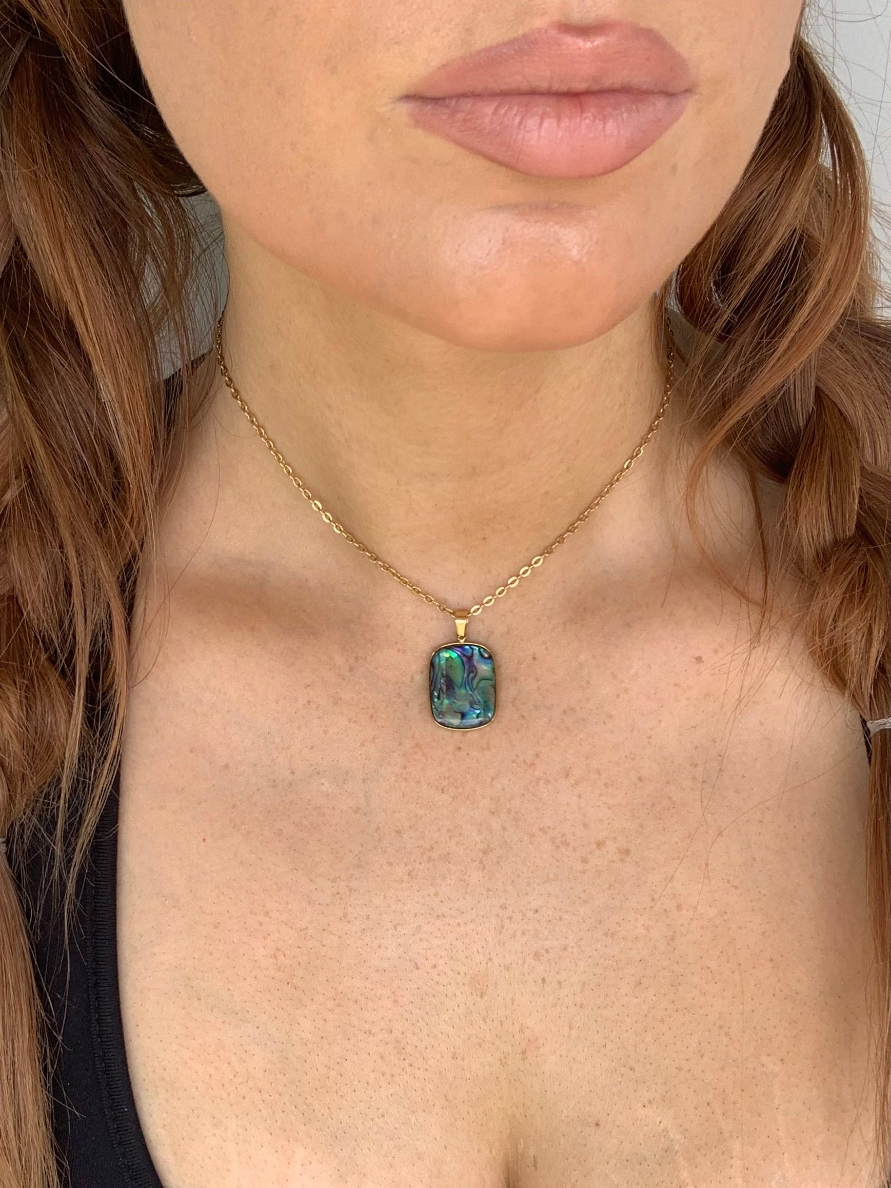 Close-up of a person wearing a gold necklace with a colorful pendant.
