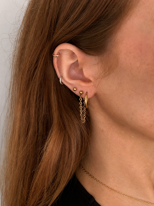 Close-up of a person wearing gold earrings and a necklace with a plain background