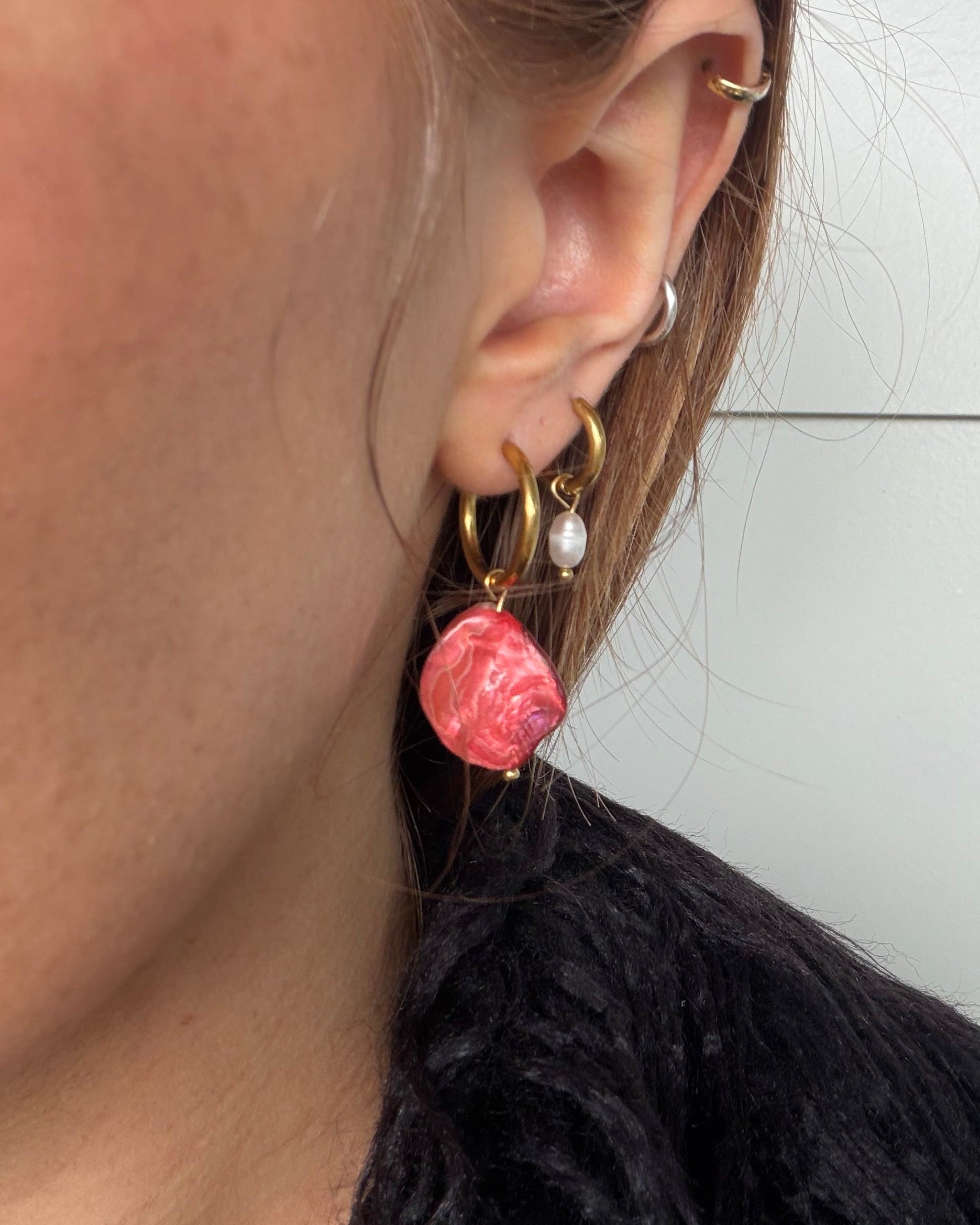 Close-up of an ear wearing a gold hoop earring with pink beads against a white background