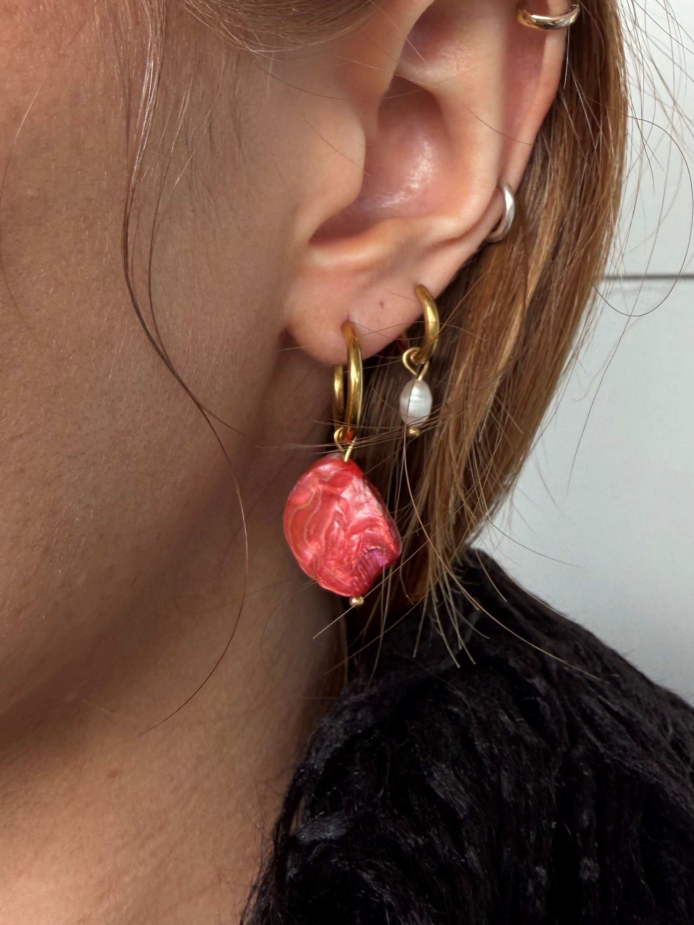 Close-up of an ear with multiple earrings against a neutral background