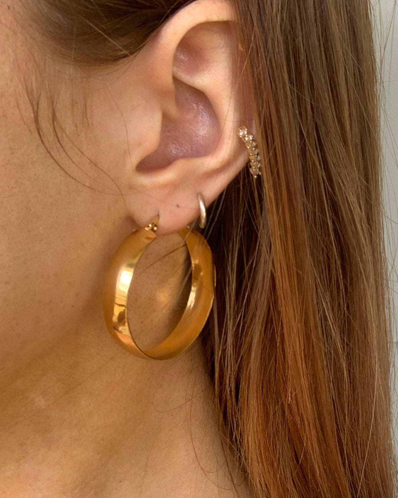 Close-up of a person wearing gold hoop earrings with a neutral background