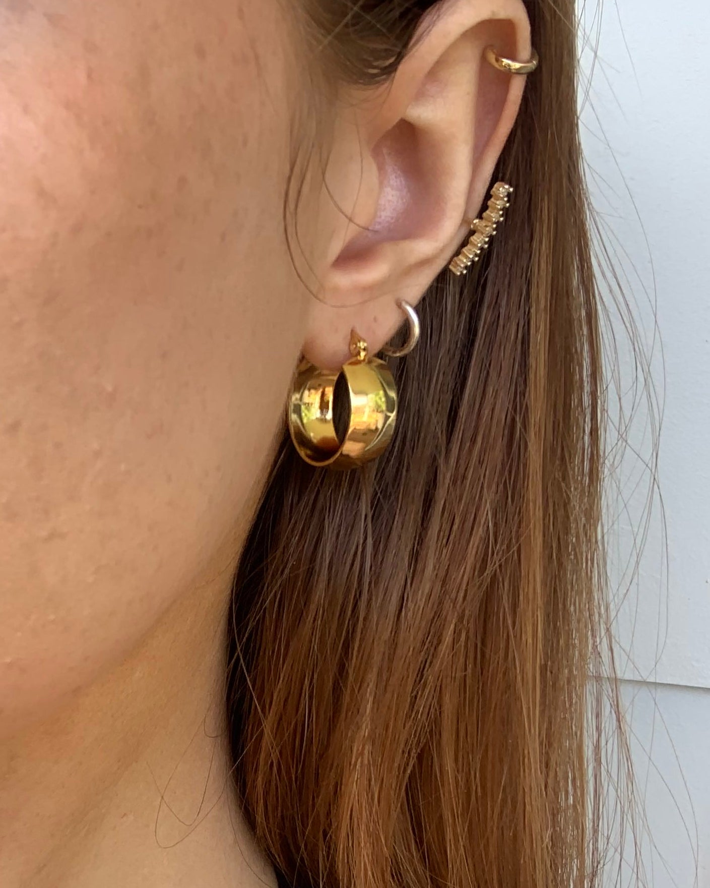 Close-up of a person wearing gold earrings with a neutral background