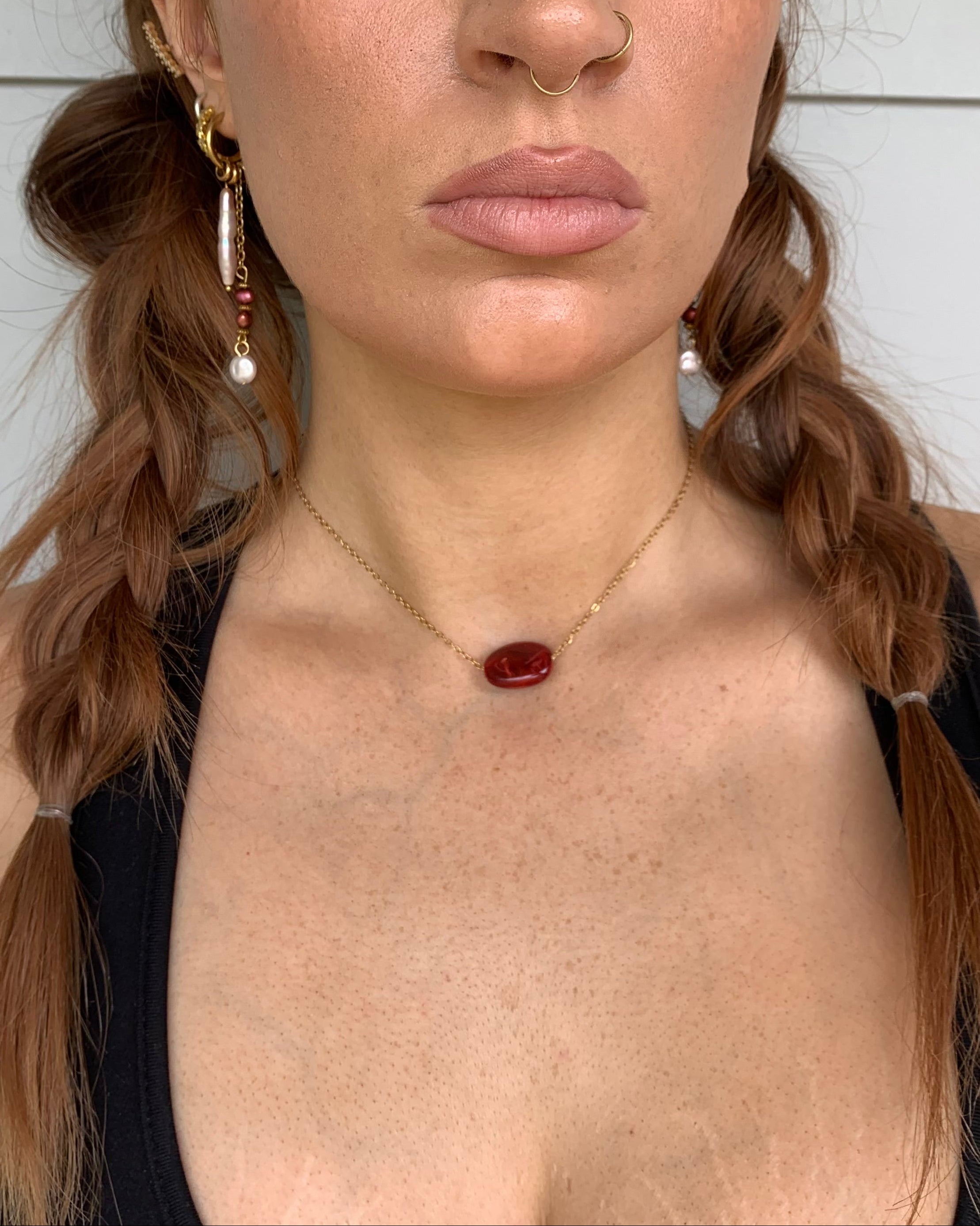 Woman wearing a necklace with a red pendant and earrings against a white background