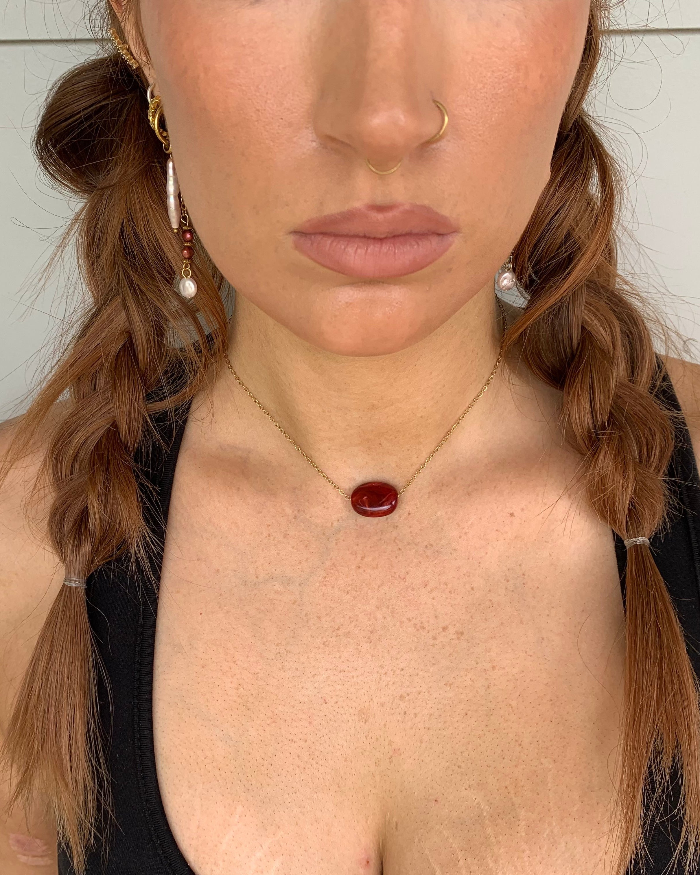 Woman wearing a necklace with a red pendant against a neutral background