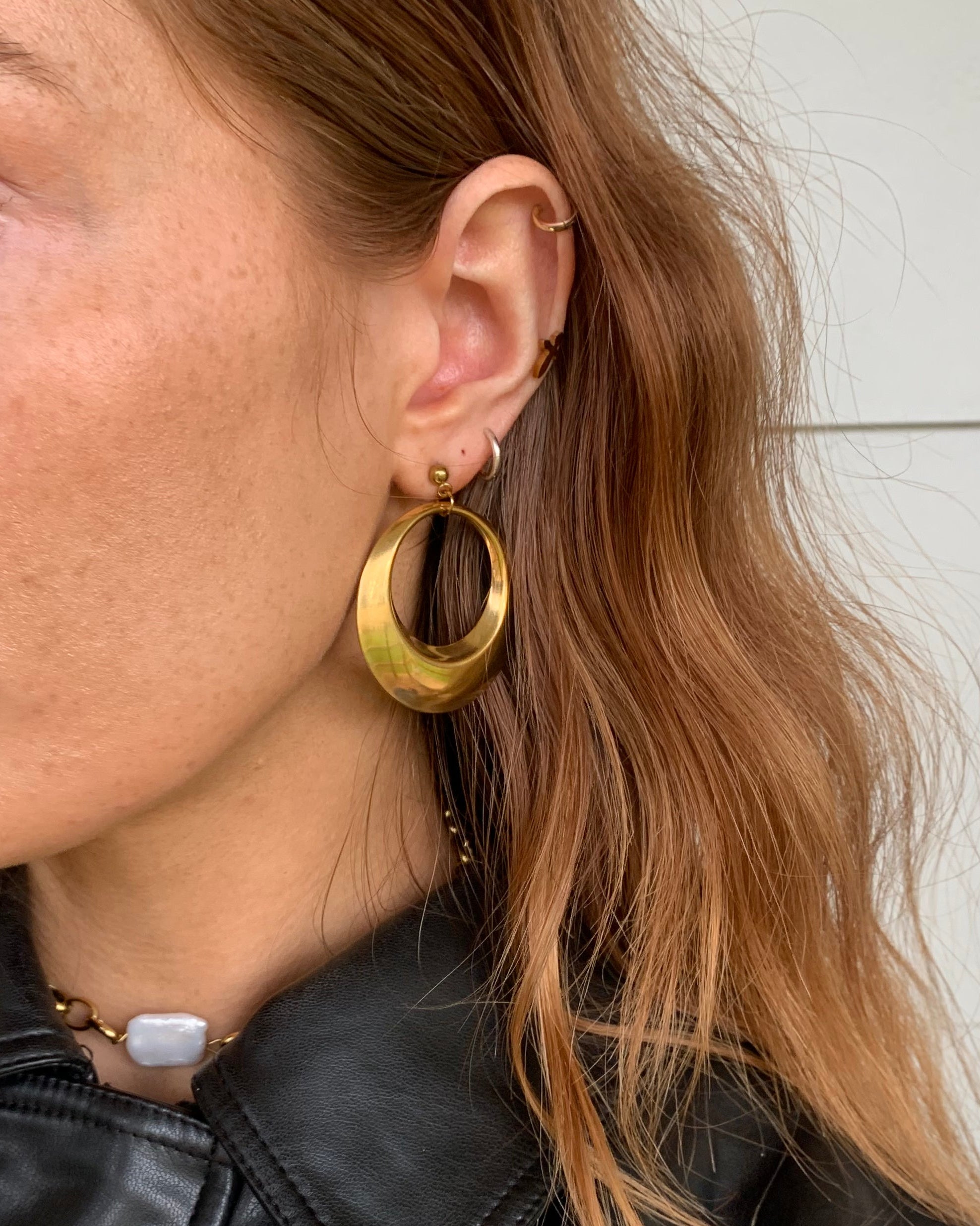 Person wearing gold hoop earrings with a black leather jacket