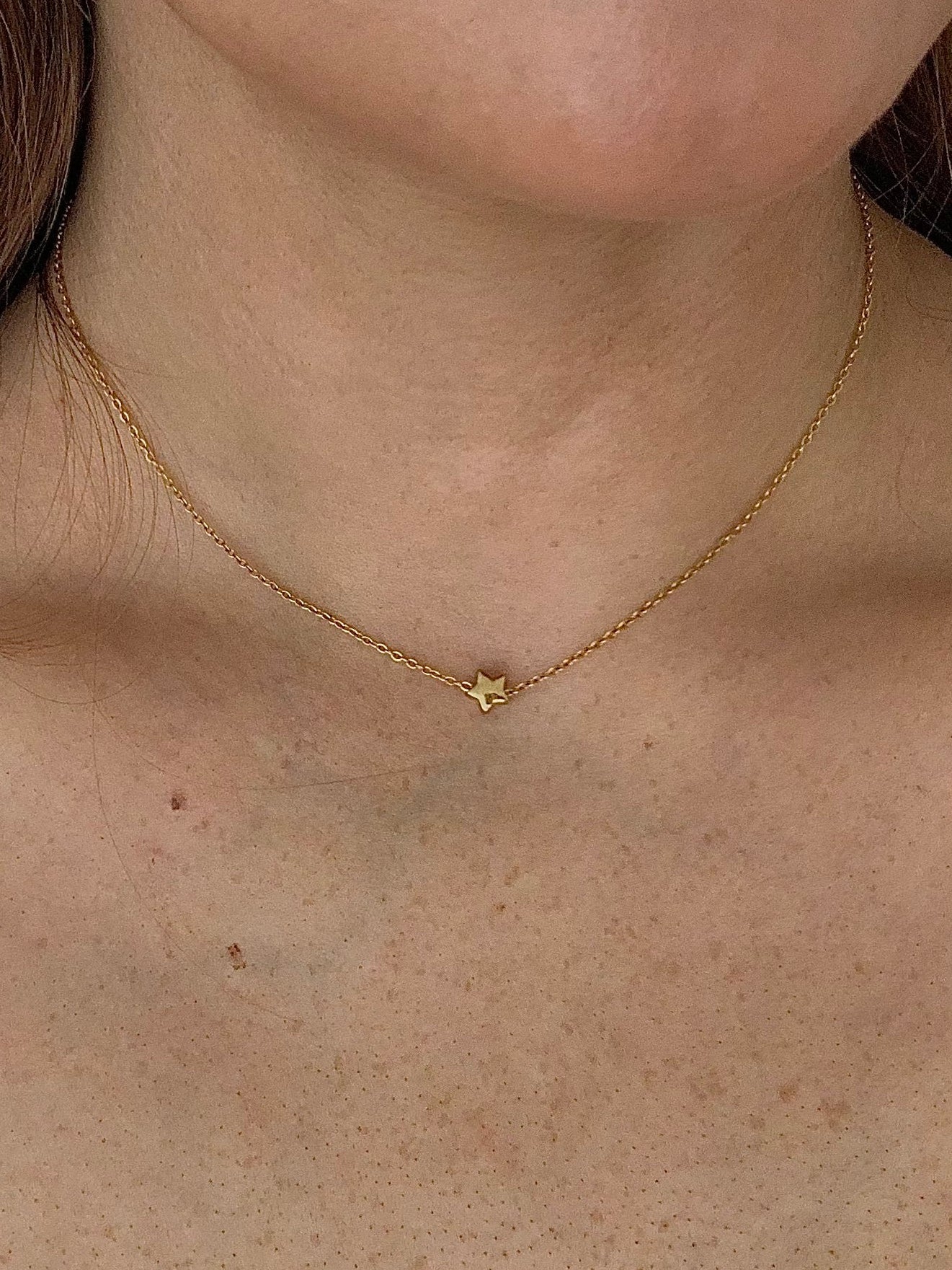 Close-up of a person wearing a gold necklace with a star pendant.