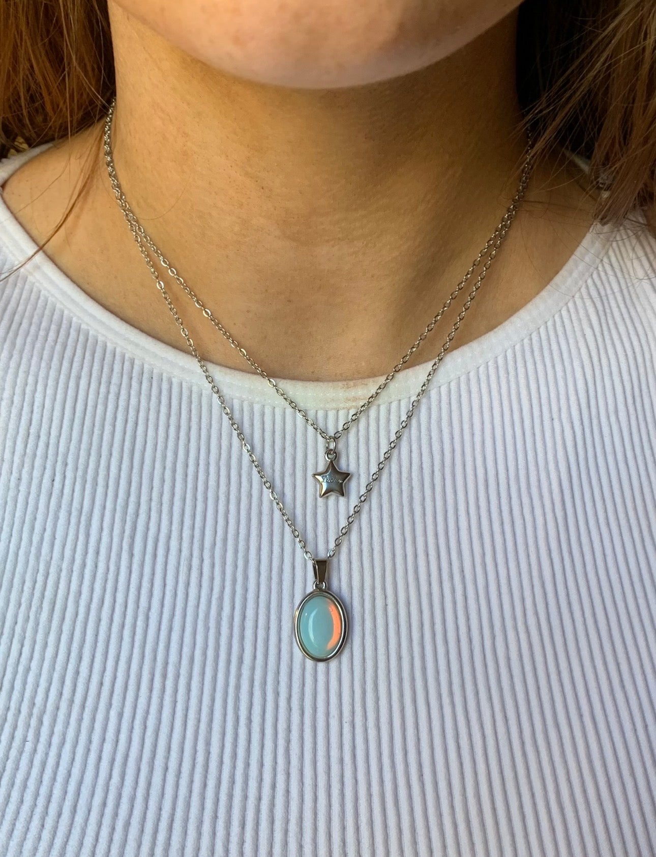Close-up of a person wearing two necklaces with pendants on a white background