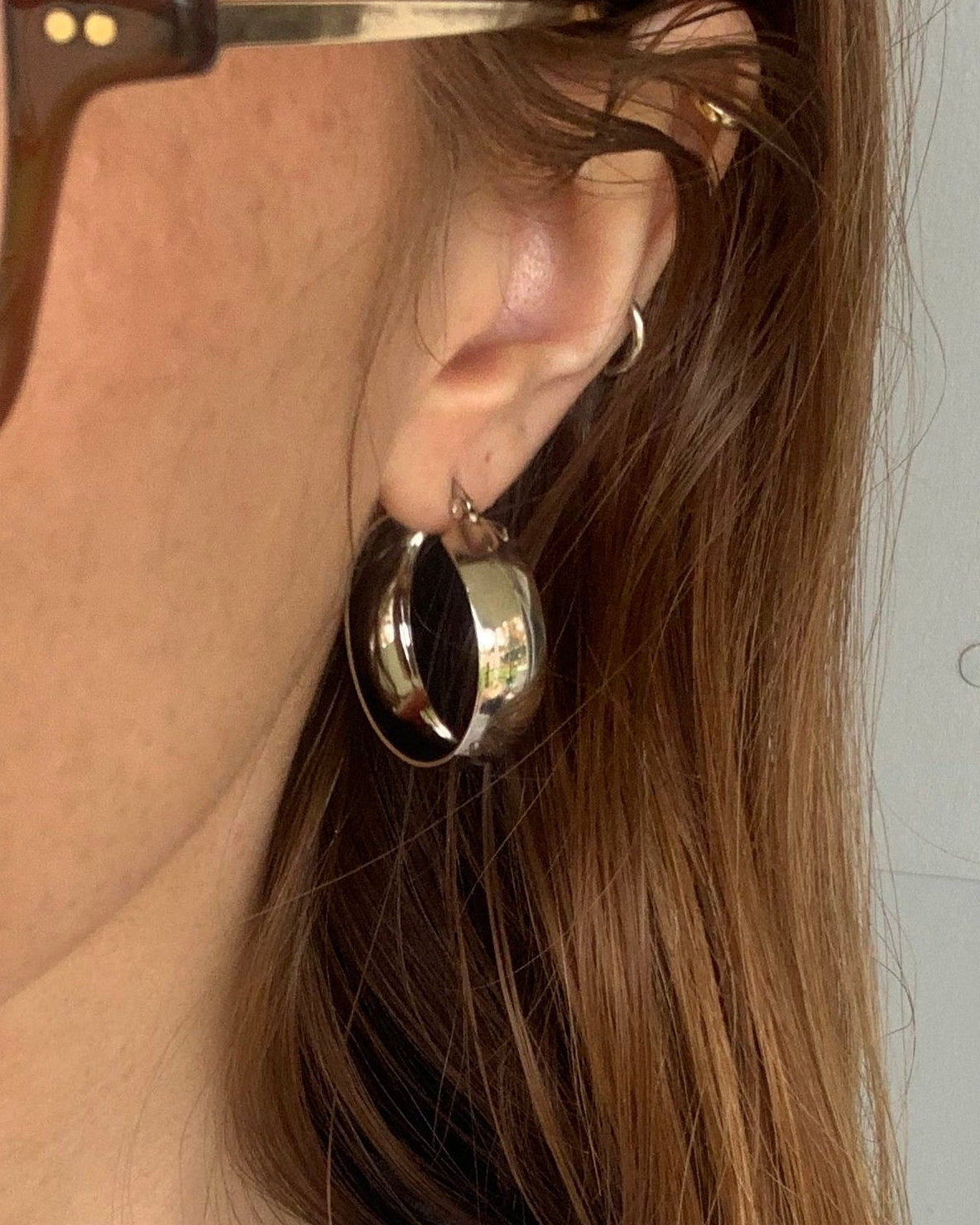 Close-up of a person wearing gold earrings and sunglasses with a tattoo on their shoulder.