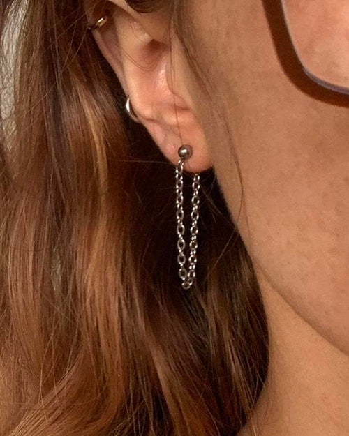 Close-up of an ear wearing a silver chain earring with a blurred background