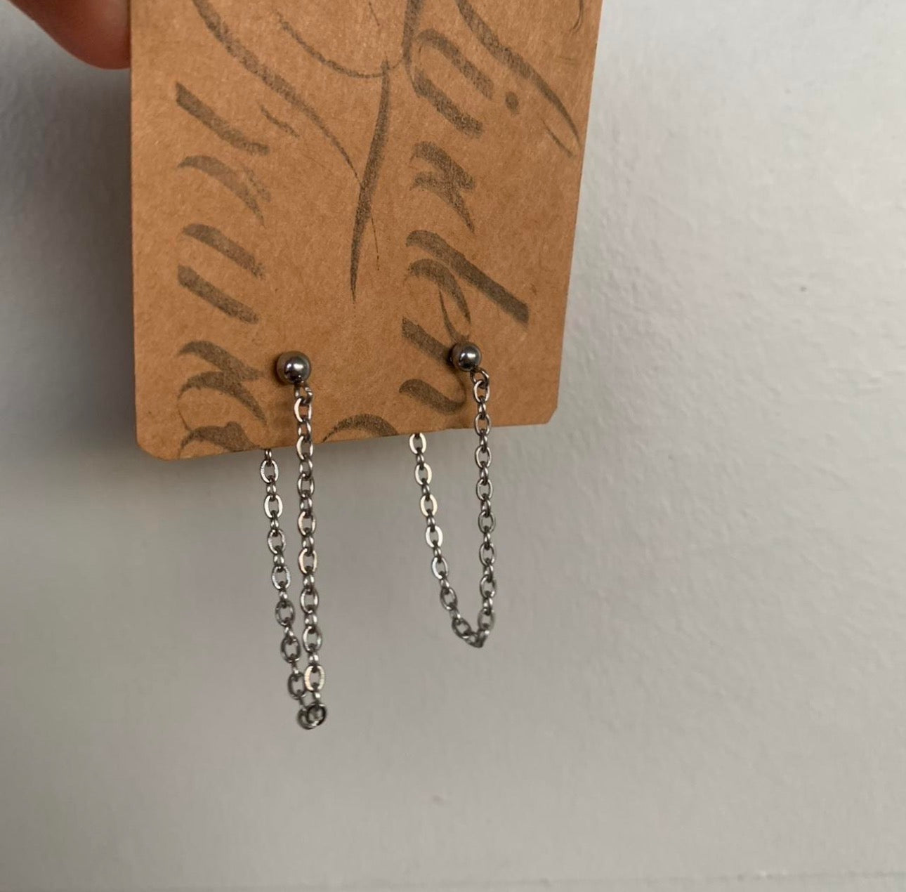 Pair of silver chain earrings on a brown card with text.