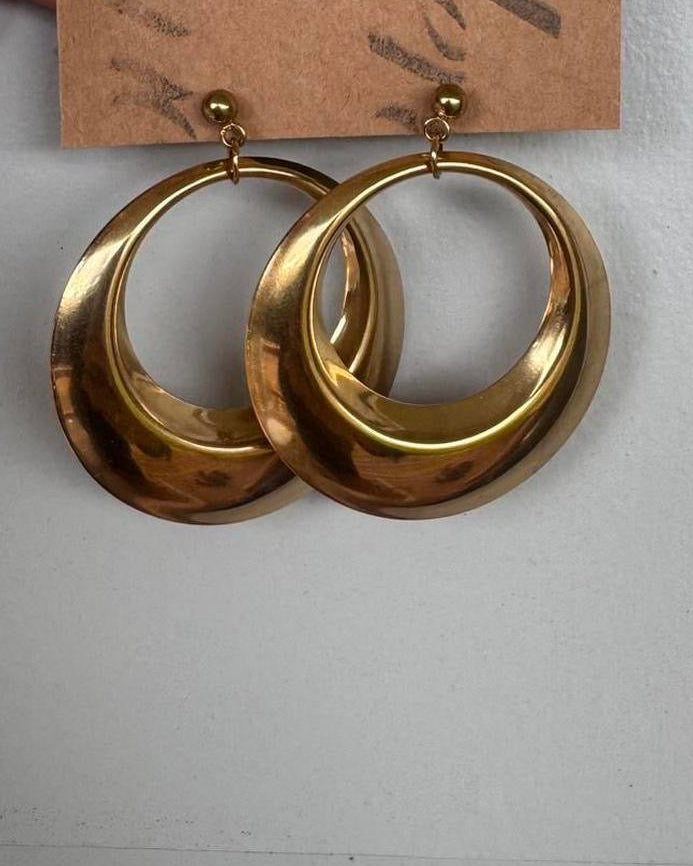 Gold hoop earrings on a cardboard tag held by a hand against a white background