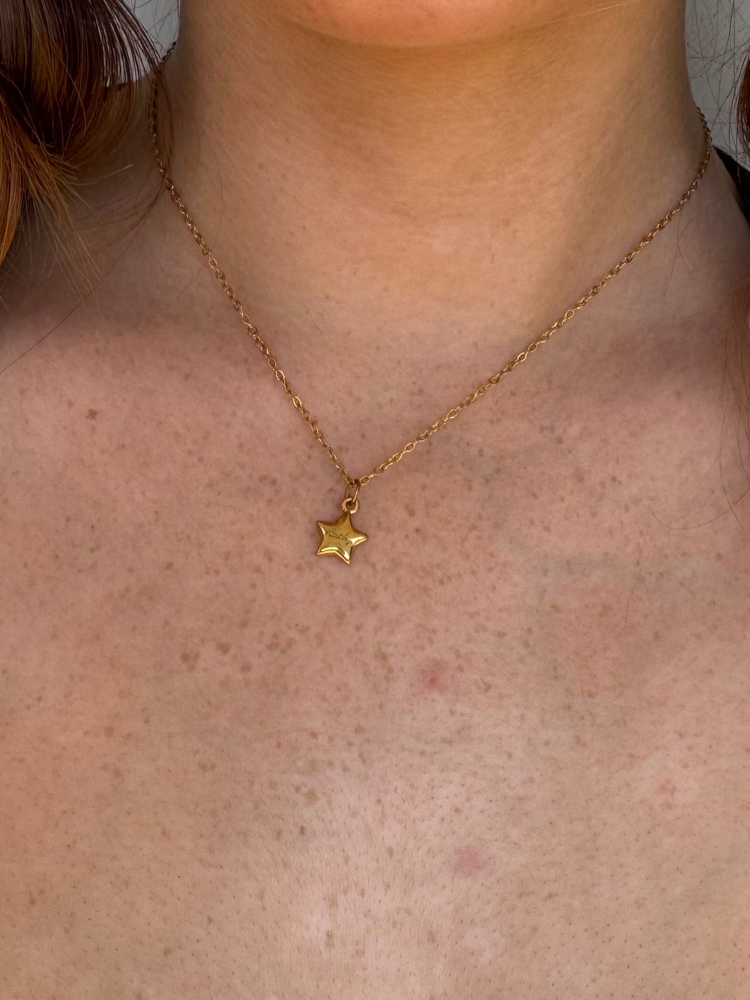 Person wearing a gold necklace with a star pendant engraved lucky.