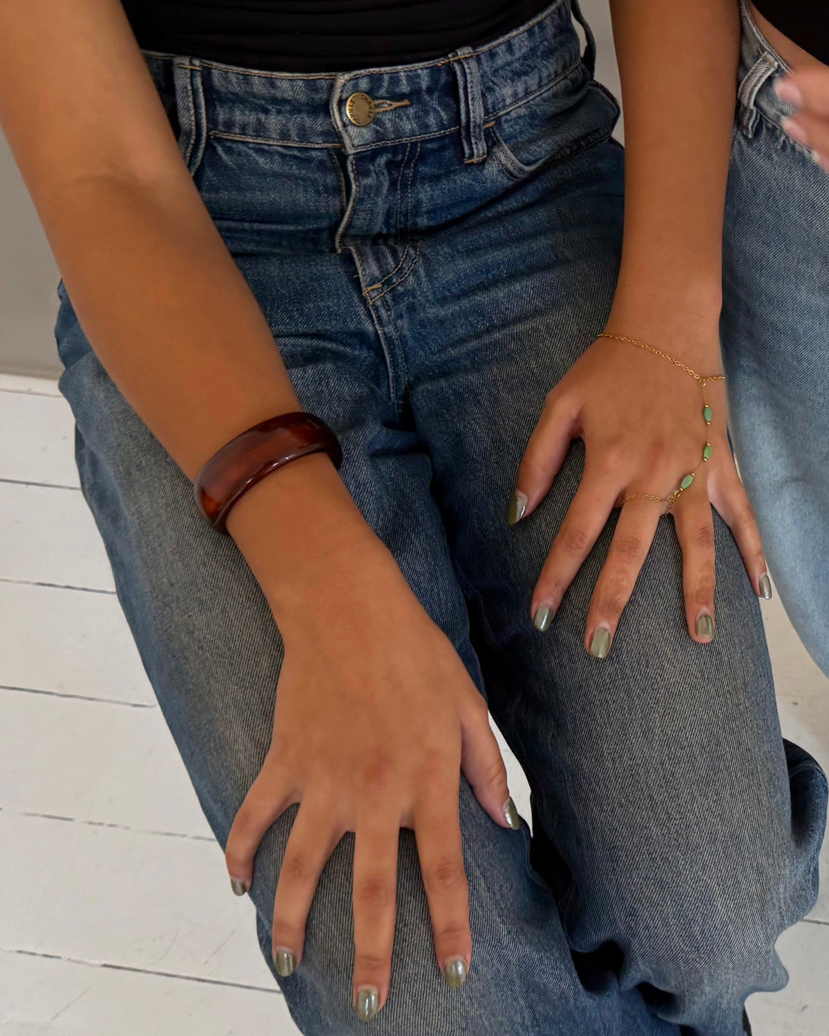 Two models wearing jeans standing on a white wooden floor. The model on the left wears a medium-wash blue straight-leg denim jacket with rolled cuffs, and the model on the right wears a light-wash blue straight-leg denim jacket with black shoes.