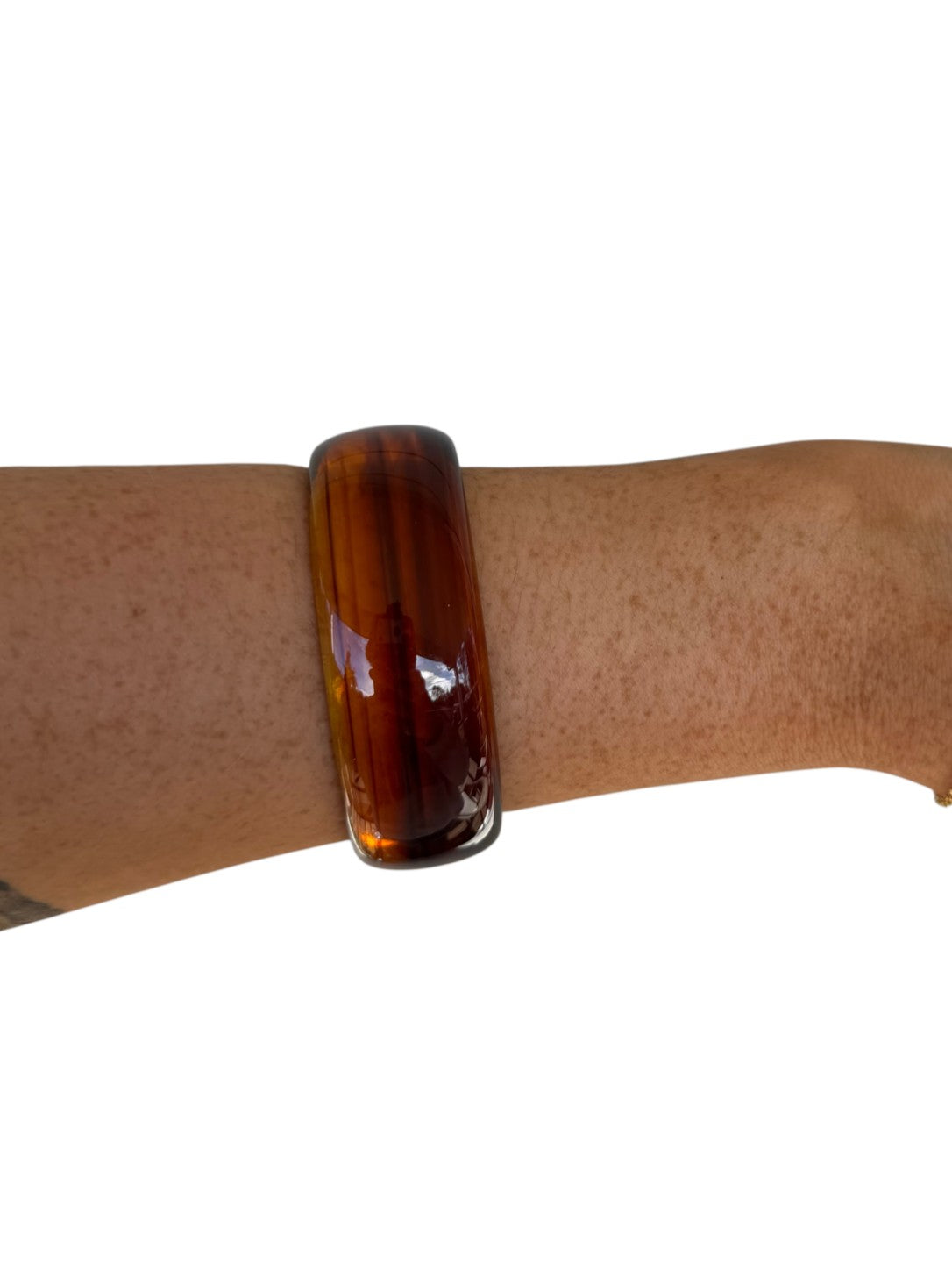 A glossy amber-brown tortoiseshell bangle bracelet worn on a person's wrist, shown against a plain white background.