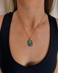 A close-up of a person wearing a gold chain necklace with a rectangular abalone shell pendant, paired with a black tank top.