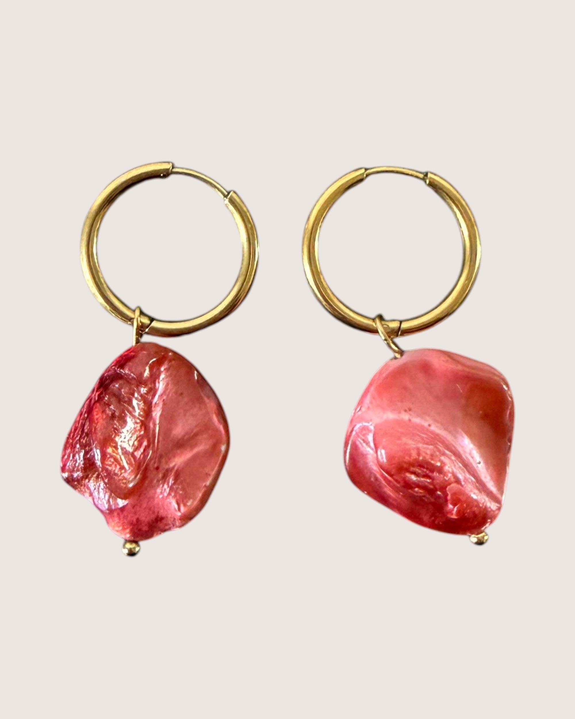 Gold hoop earrings with pink stone drops on a light background