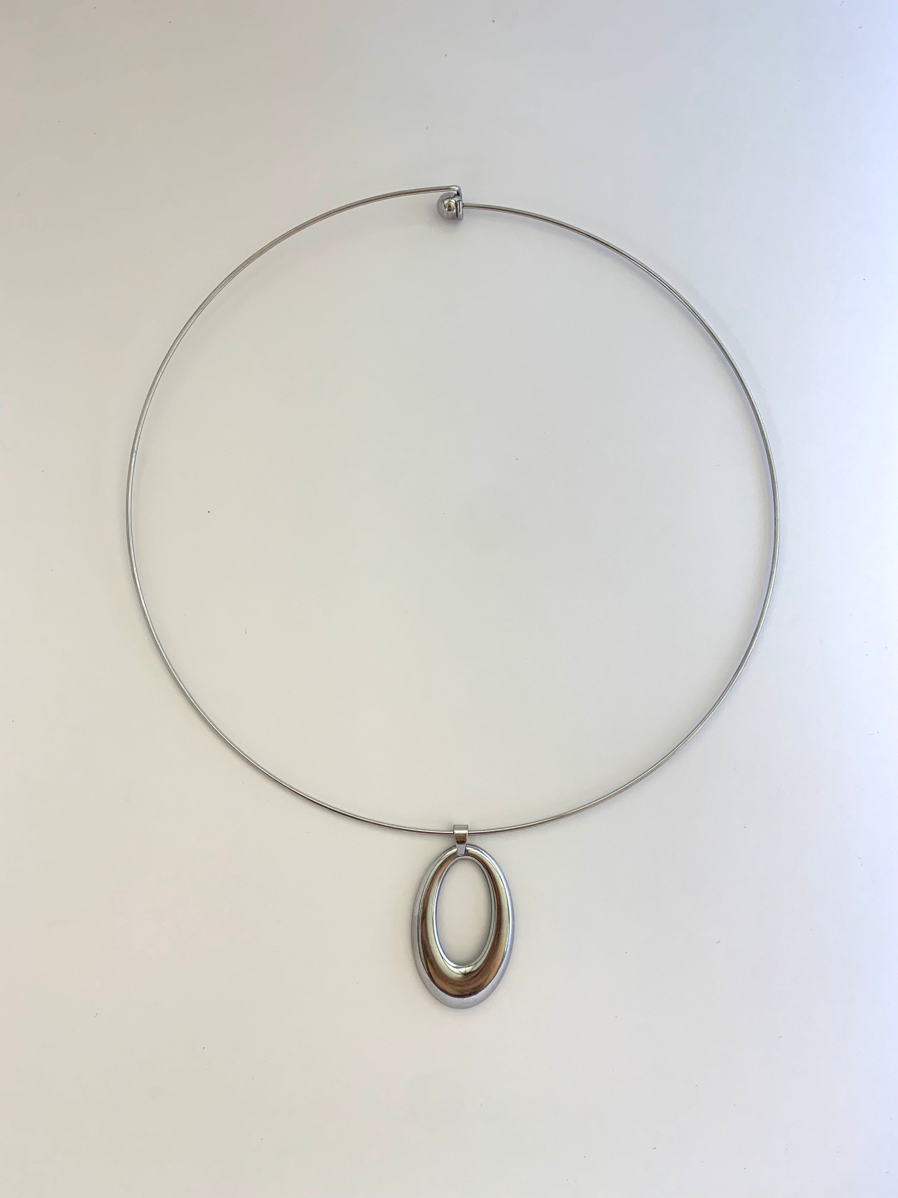 A minimalist silver wire necklace with a double-ring oval pendant, displayed against a plain off-white background.
