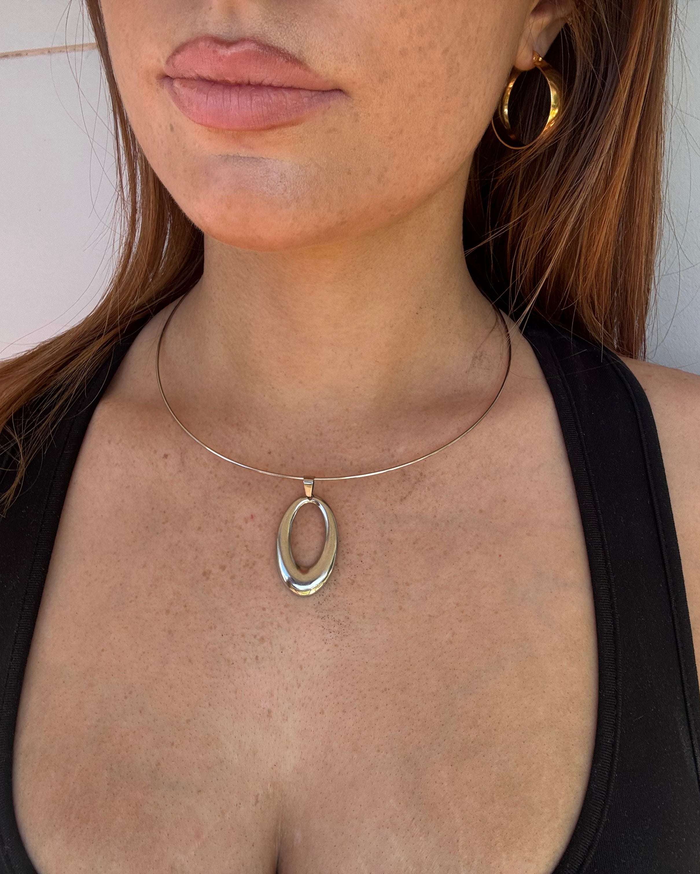 A close-up of a person's and neck wearing a delicate silver-toned circular wire necklace with oval stainless steel pendant.