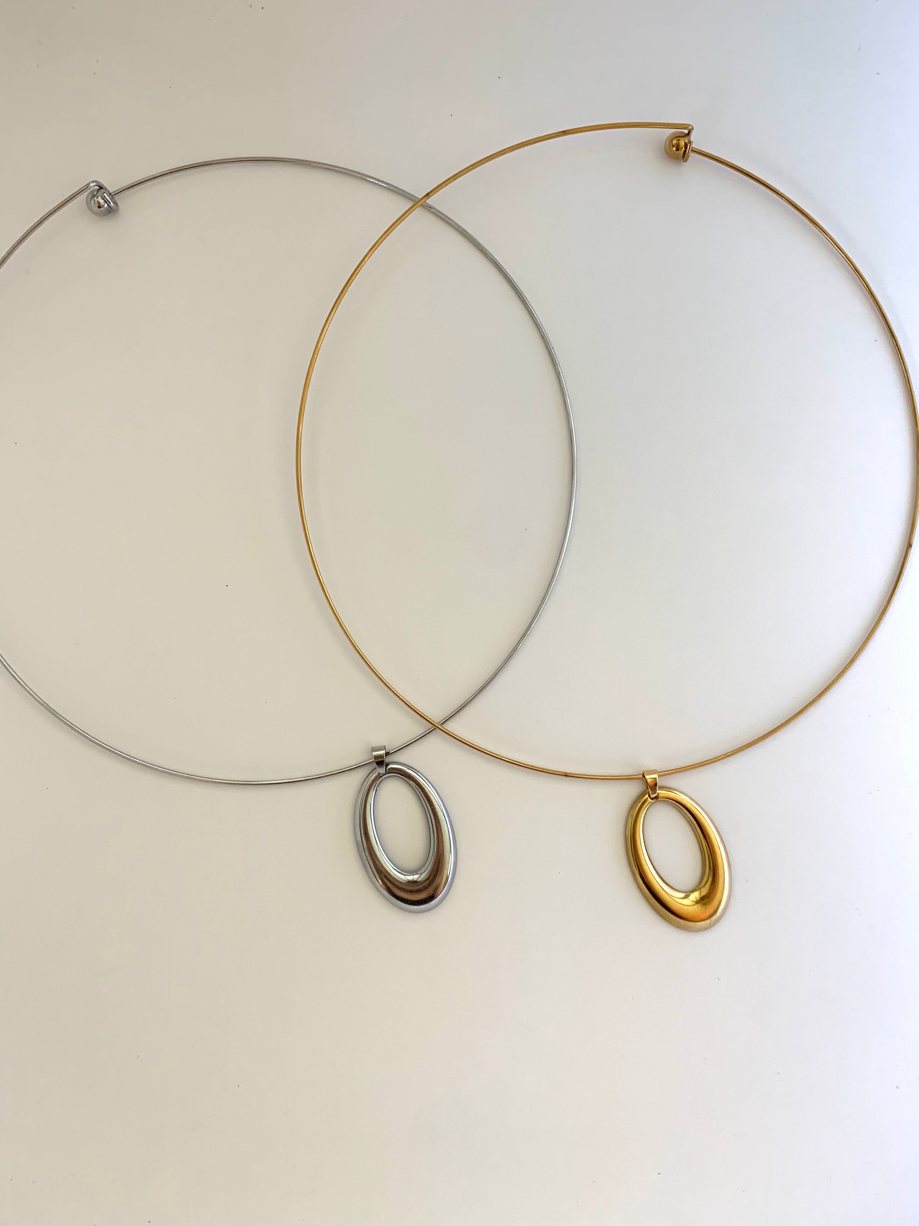 Two minimalist wire hoop necklaces with oval pendants, one in silver and one in gold, displayed on a plain off-white background.