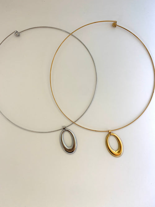 Two minimalist wire hoop necklaces with oval pendants, one in silver and one in gold, displayed on a plain off-white background.