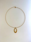 A minimalist gold wire necklace with a polished oval pendant, displayed against a clean off-white background.