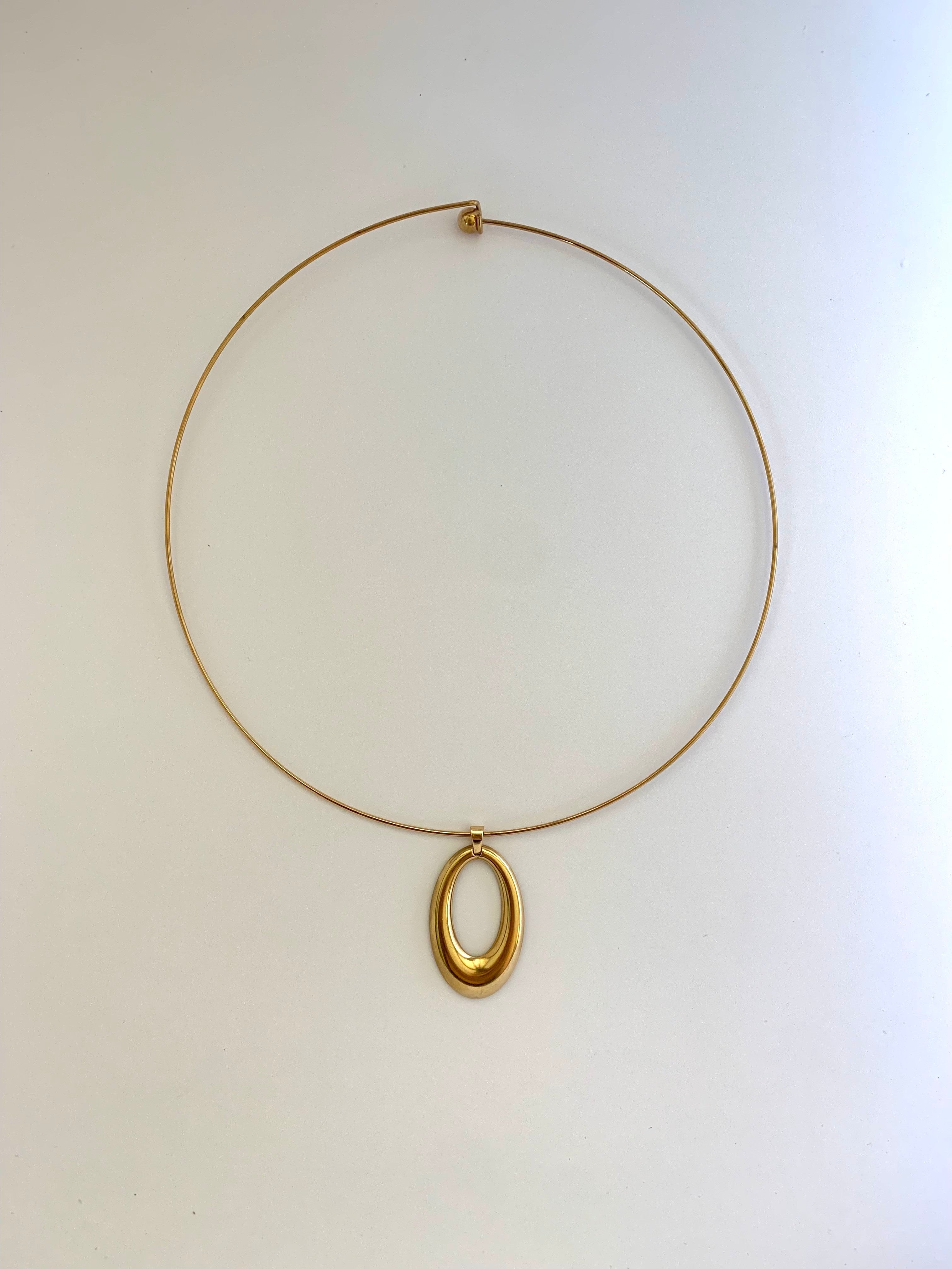 A minimalist gold wire necklace with a polished oval pendant, displayed against a clean off-white background.