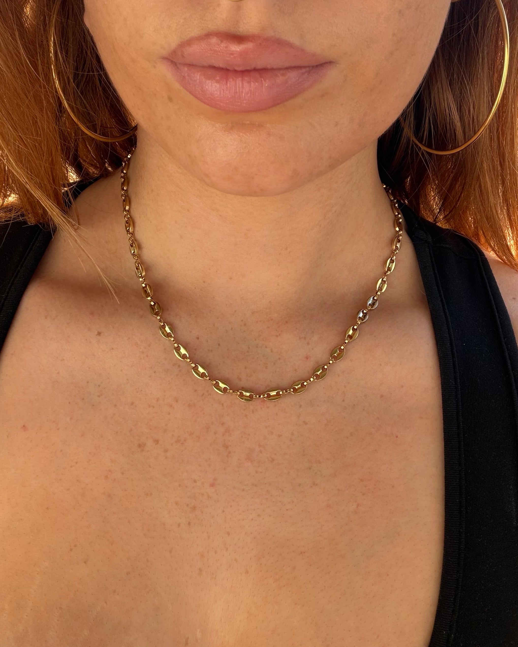 Close-up of a person wearing a gold chain necklace with a blurred background