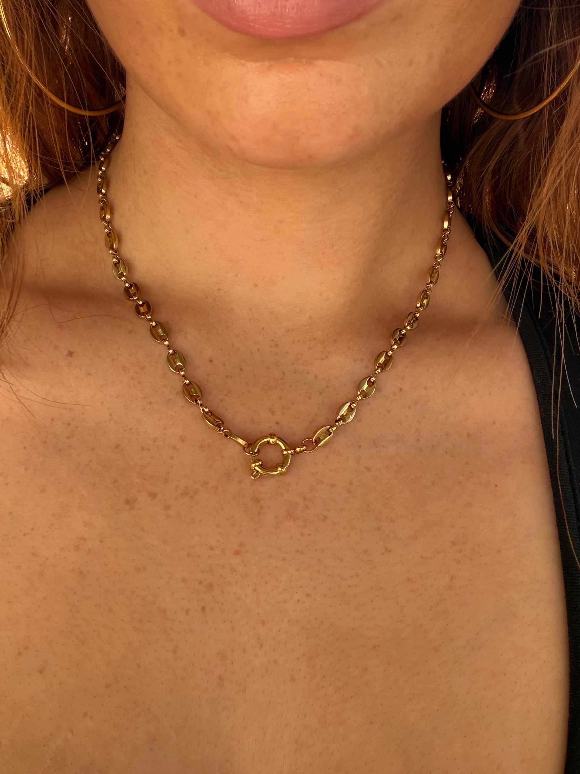Close-up of a person wearing a gold chain necklace with a blurred background