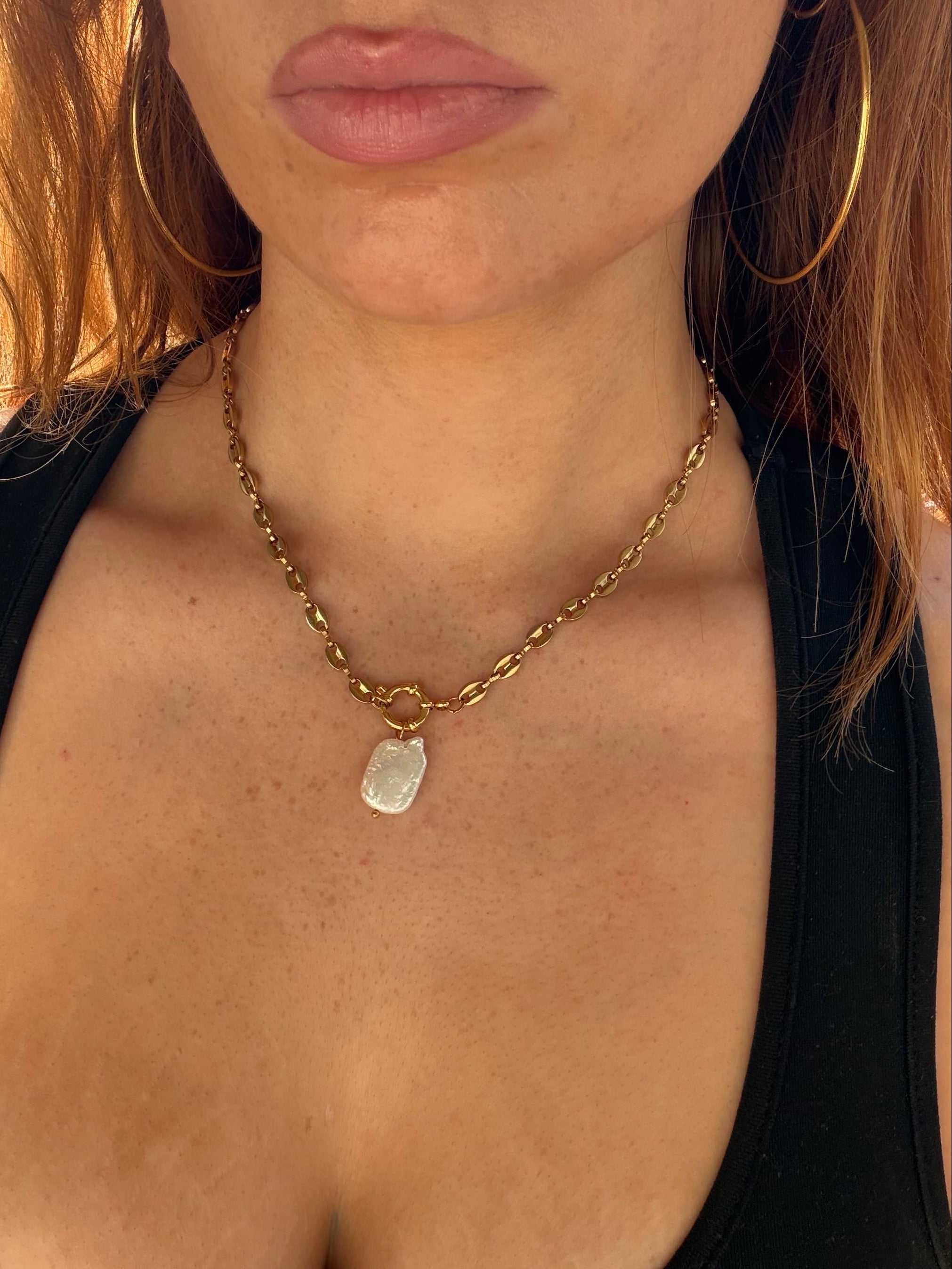 Close-up of a person wearing a gold chain necklace with a pendant.