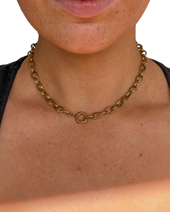 A close-up of a person wearing a gold-toned chain necklace with a circular link detail, paired with a black tank top against a plain white background.
