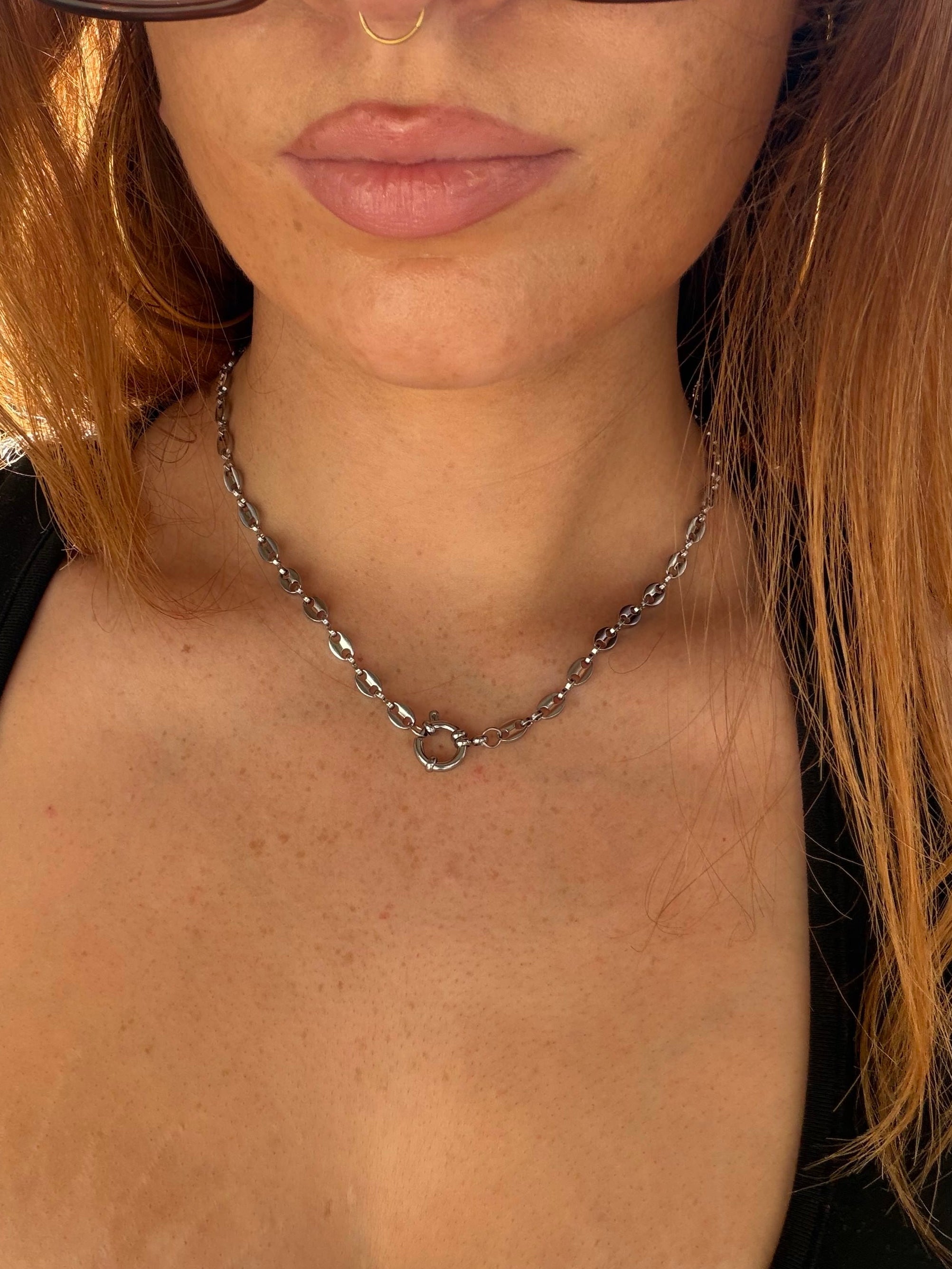 Close-up of a person wearing glasses and a necklace with a blurred background