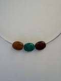 Three polished oval beads in dark red, green, and brown arranged vertically on a thin silver wire against a plain light background.