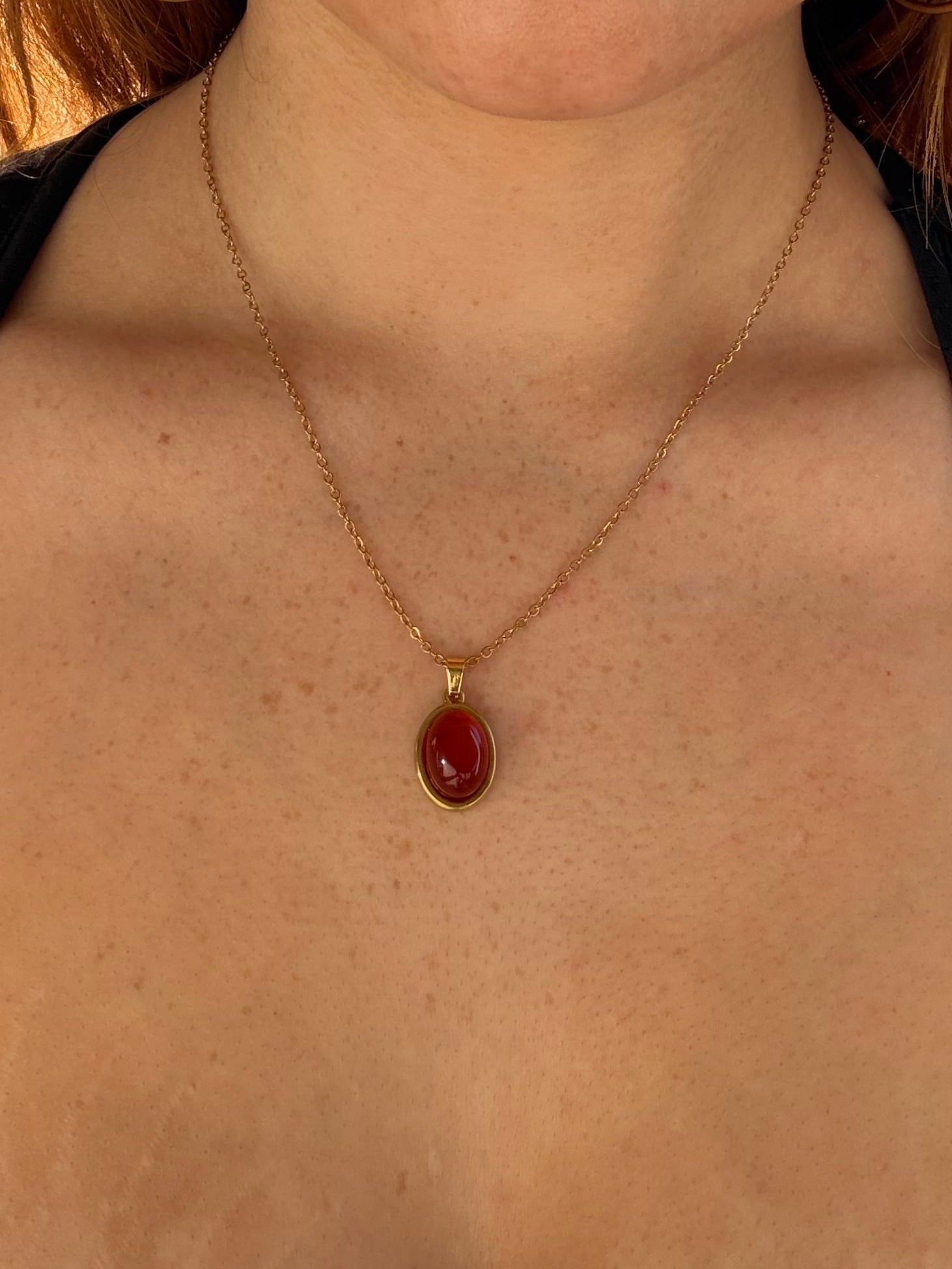 Close-up of a person wearing a gold necklace with a red pendant.