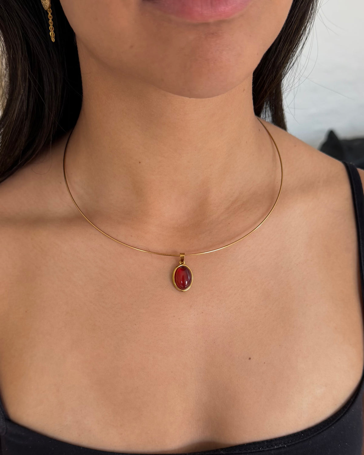 A close-up of a model wearing a delicate gold cable necklace with an oval red gemstone pendant.
