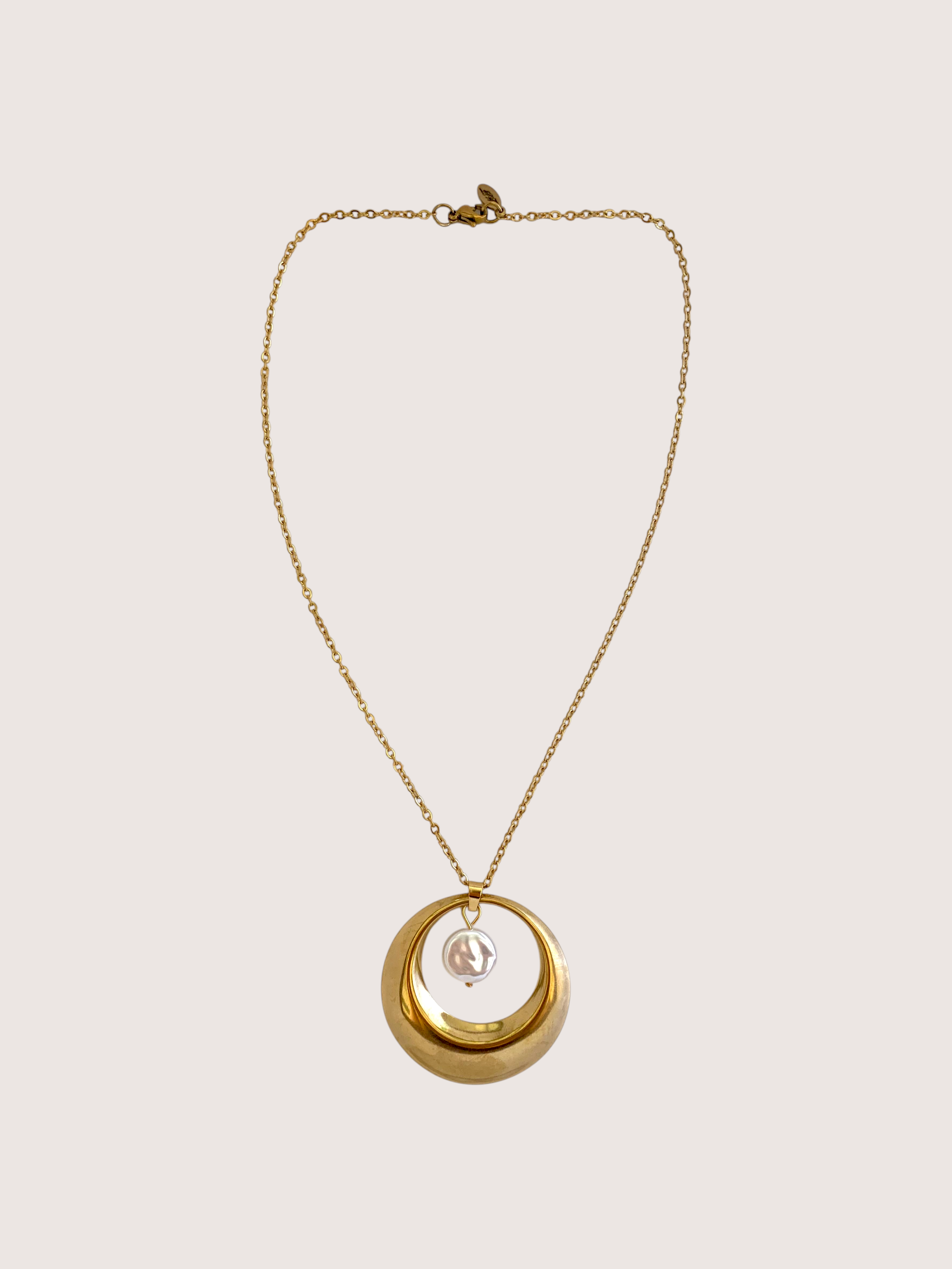 Gold necklace with a circular pendant on a light beige background