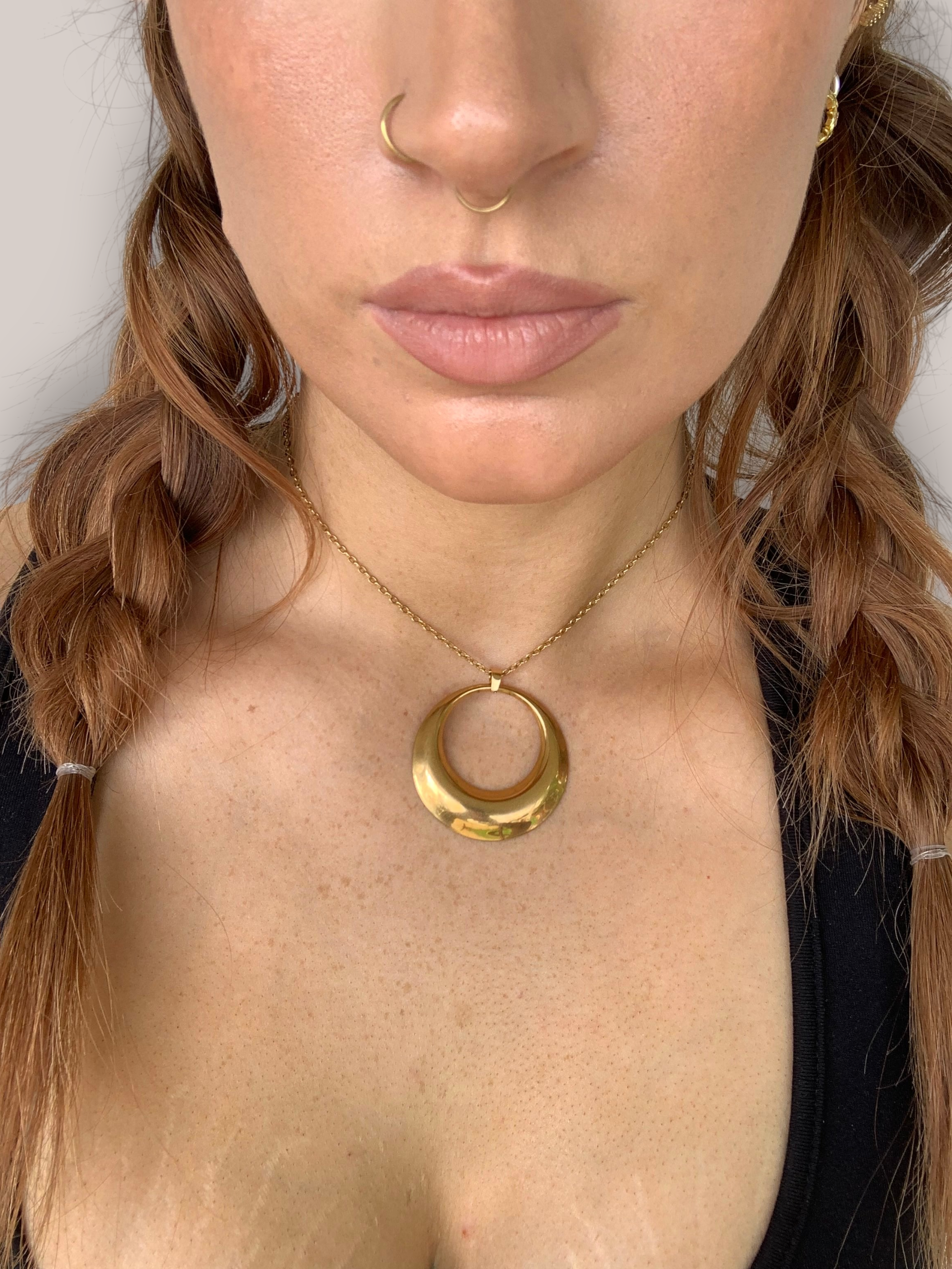 Close-up of a person wearing a gold necklace with a large circular pendant.