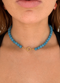 Close-up of a person wearing a turquoise beaded necklace with a gold clasp.