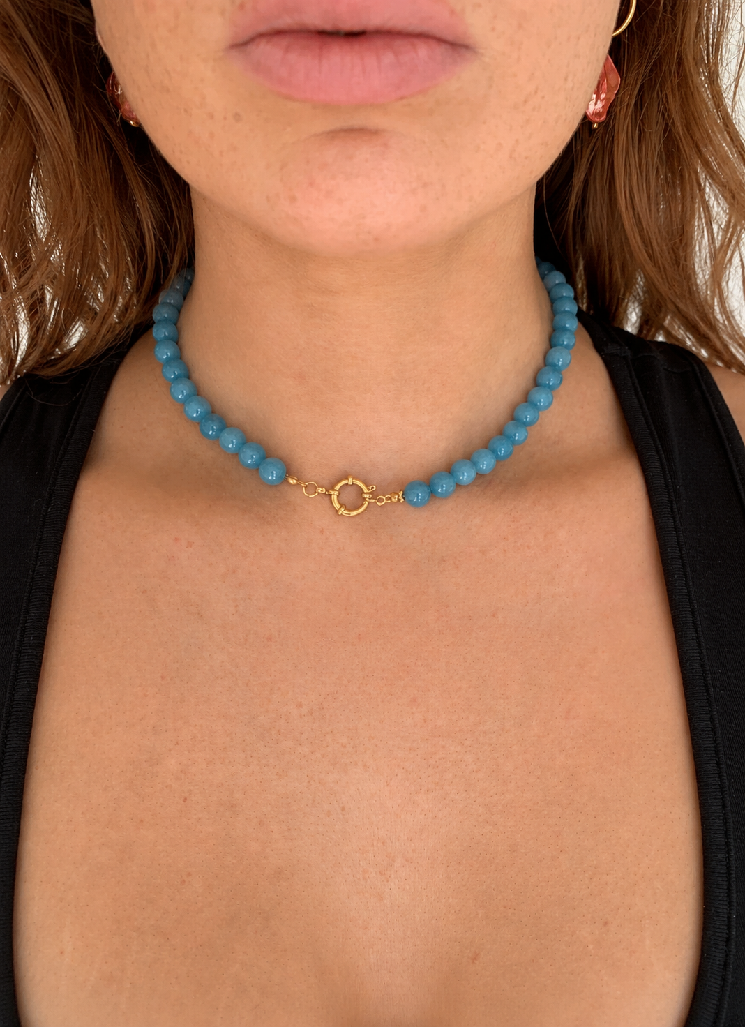 Close-up of a person wearing a turquoise beaded necklace with a gold clasp.