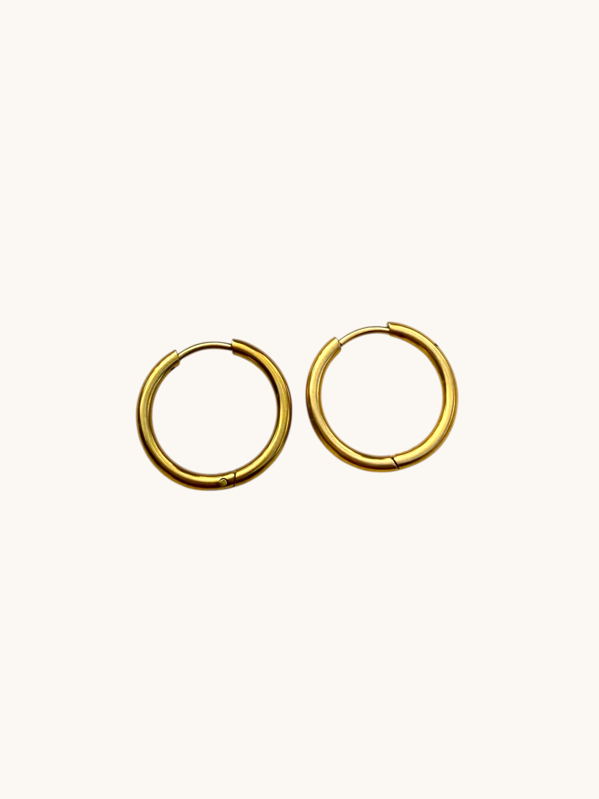 A pair of small gold hoop earrings on a plain off-white background.