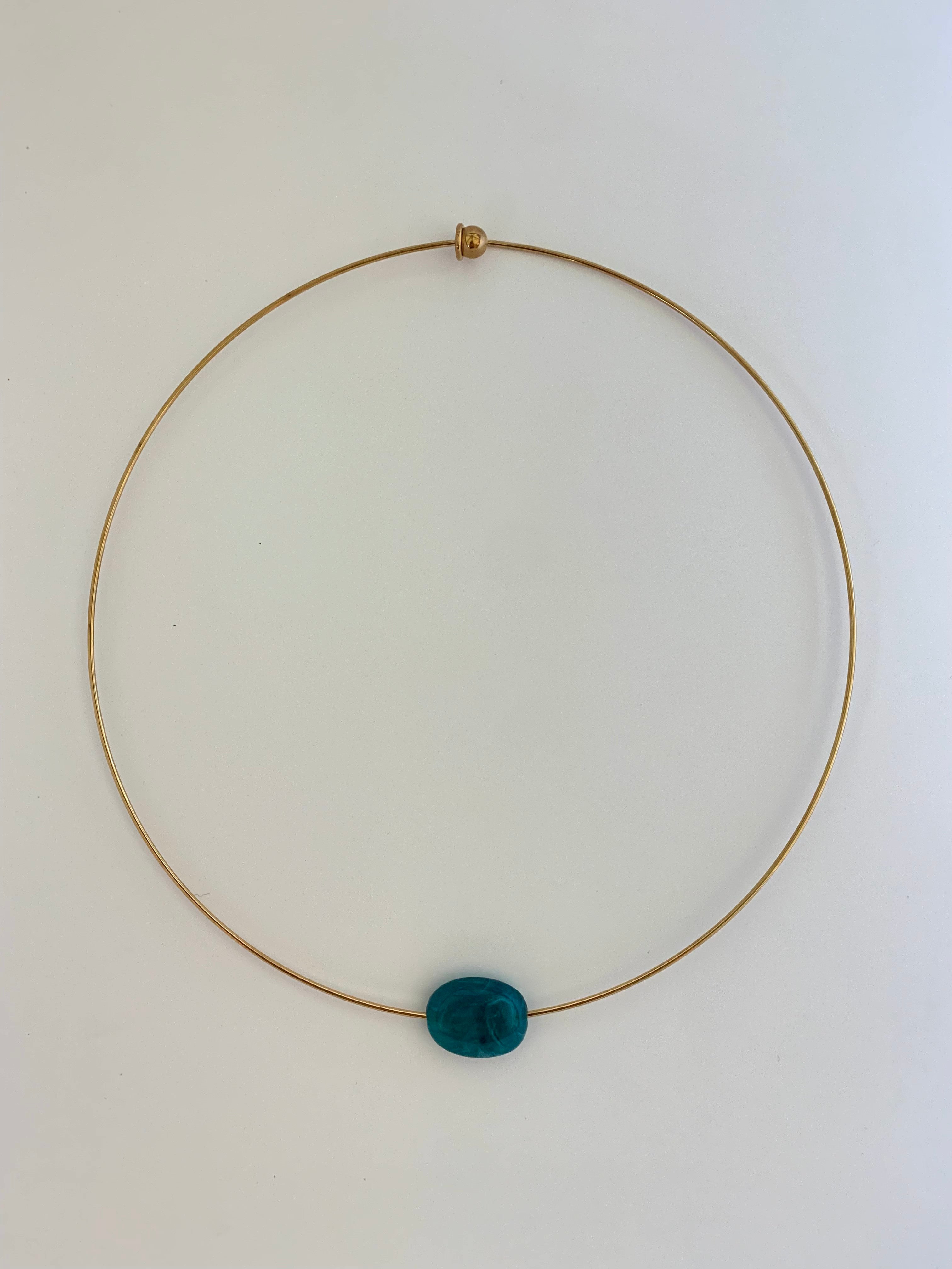 A delicate gold wire necklace with a single oval dark teal blue bead pendant, displayed on a plain white background.
