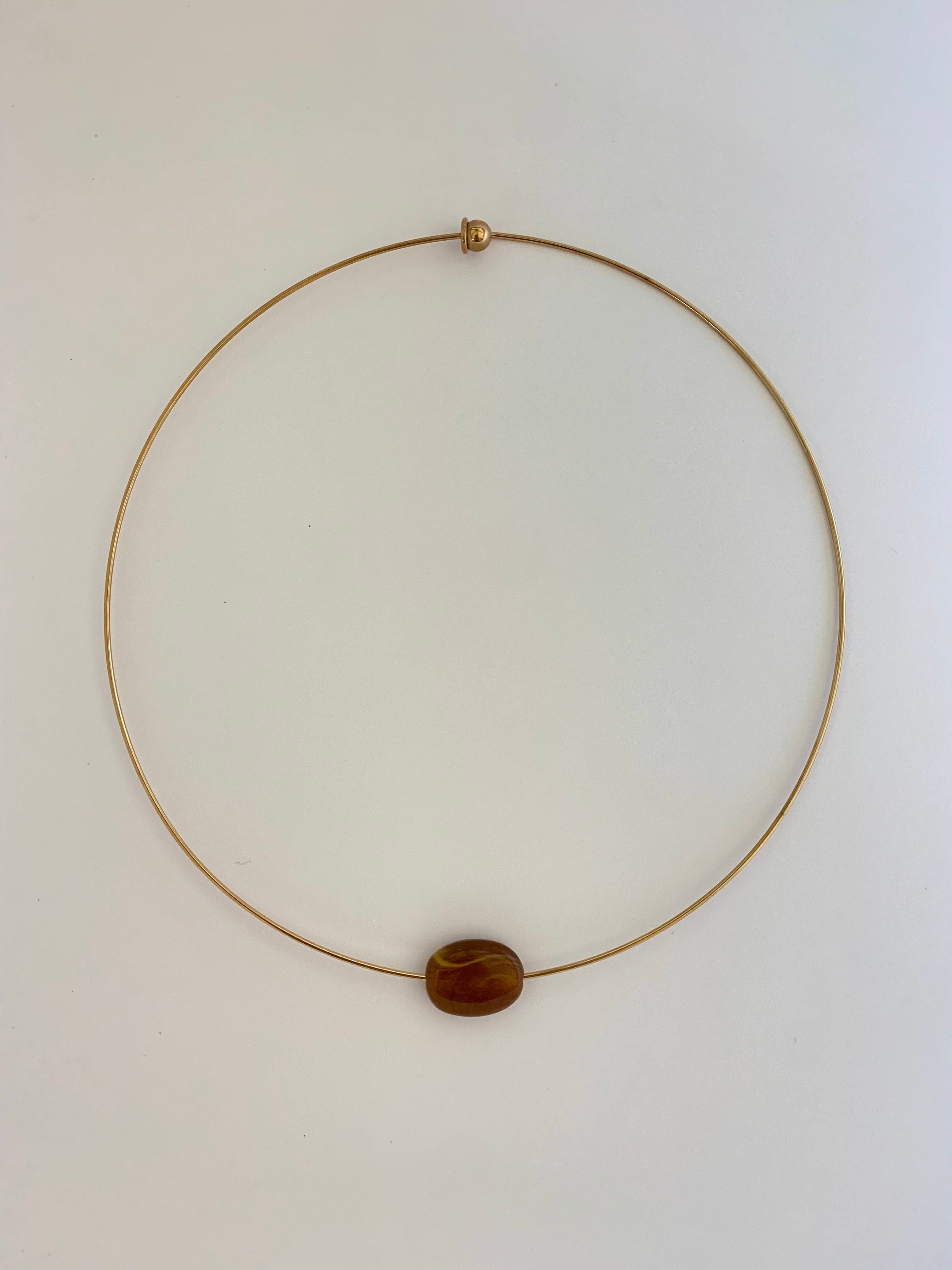 A delicate gold wire necklace with a single polished brown stone bead pendant, displayed on a clean white background.