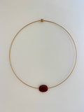 A delicate gold wire necklace with a single oval dark red gemstone pendant, displayed on a plain white background.