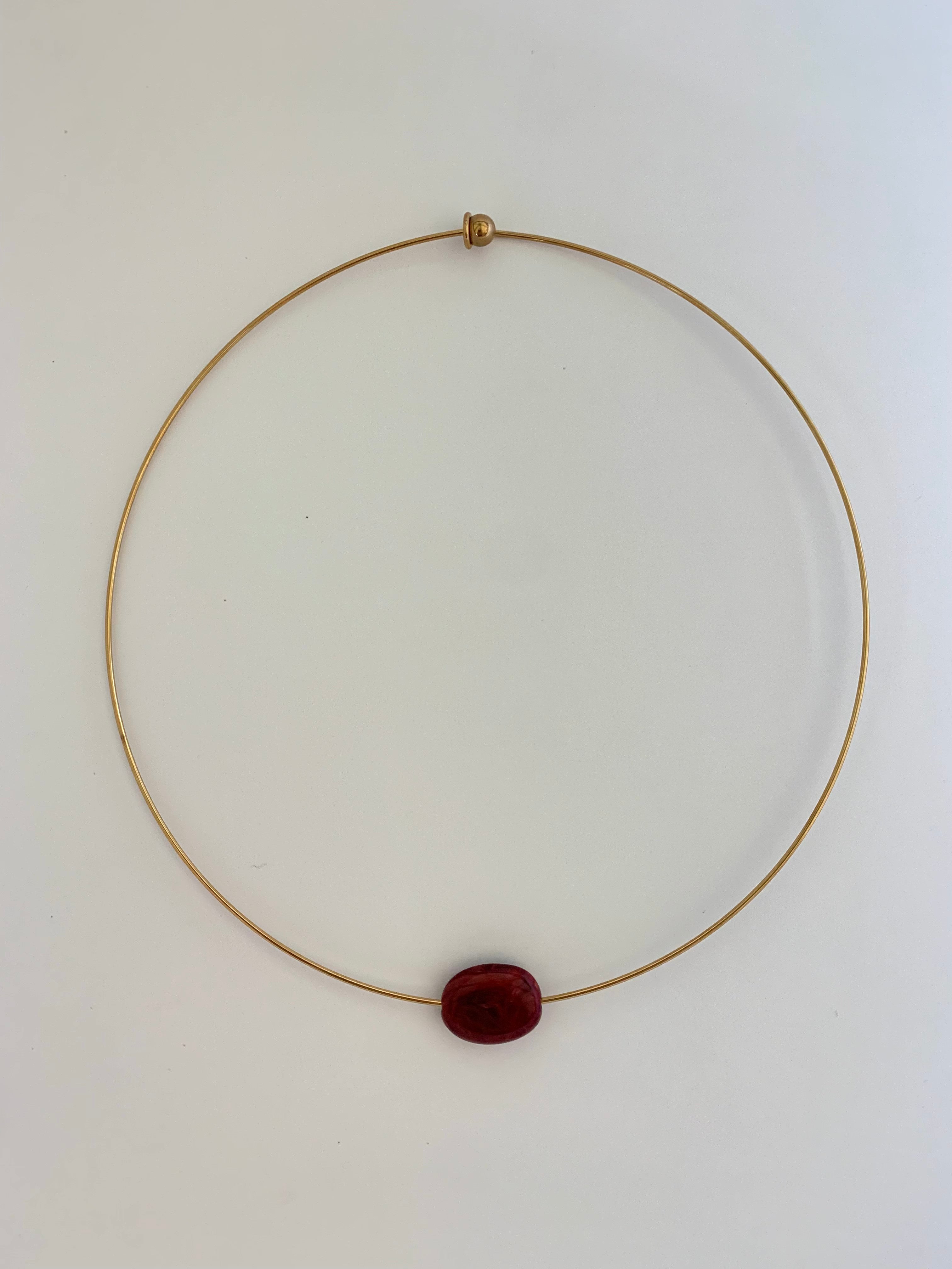 A delicate gold wire necklace with a single oval dark red gemstone pendant, displayed on a plain white background.