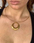 A close-up of a model's chest and neck area wearing a gold ring pendant necklace with a thin gold wire loop extending from the bottom of the ring.