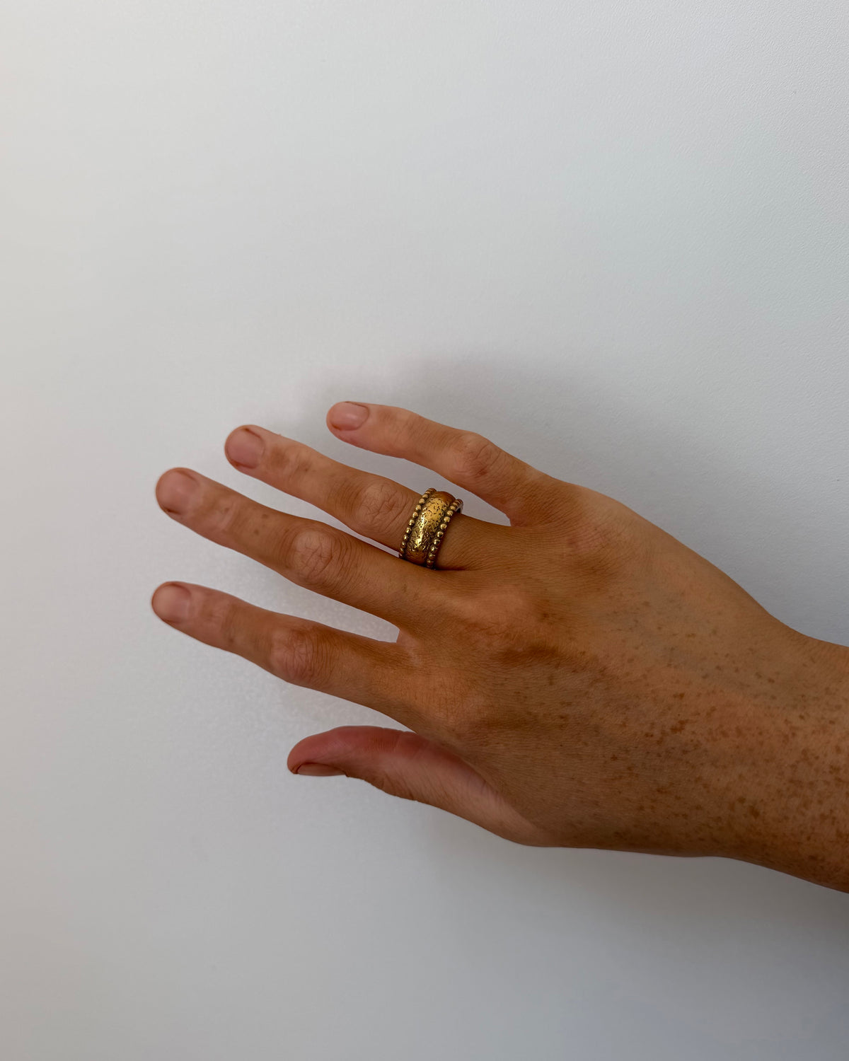 A gold ring with a textured, hammered band worn on a person's ring finger, shown against a plain light gray background.