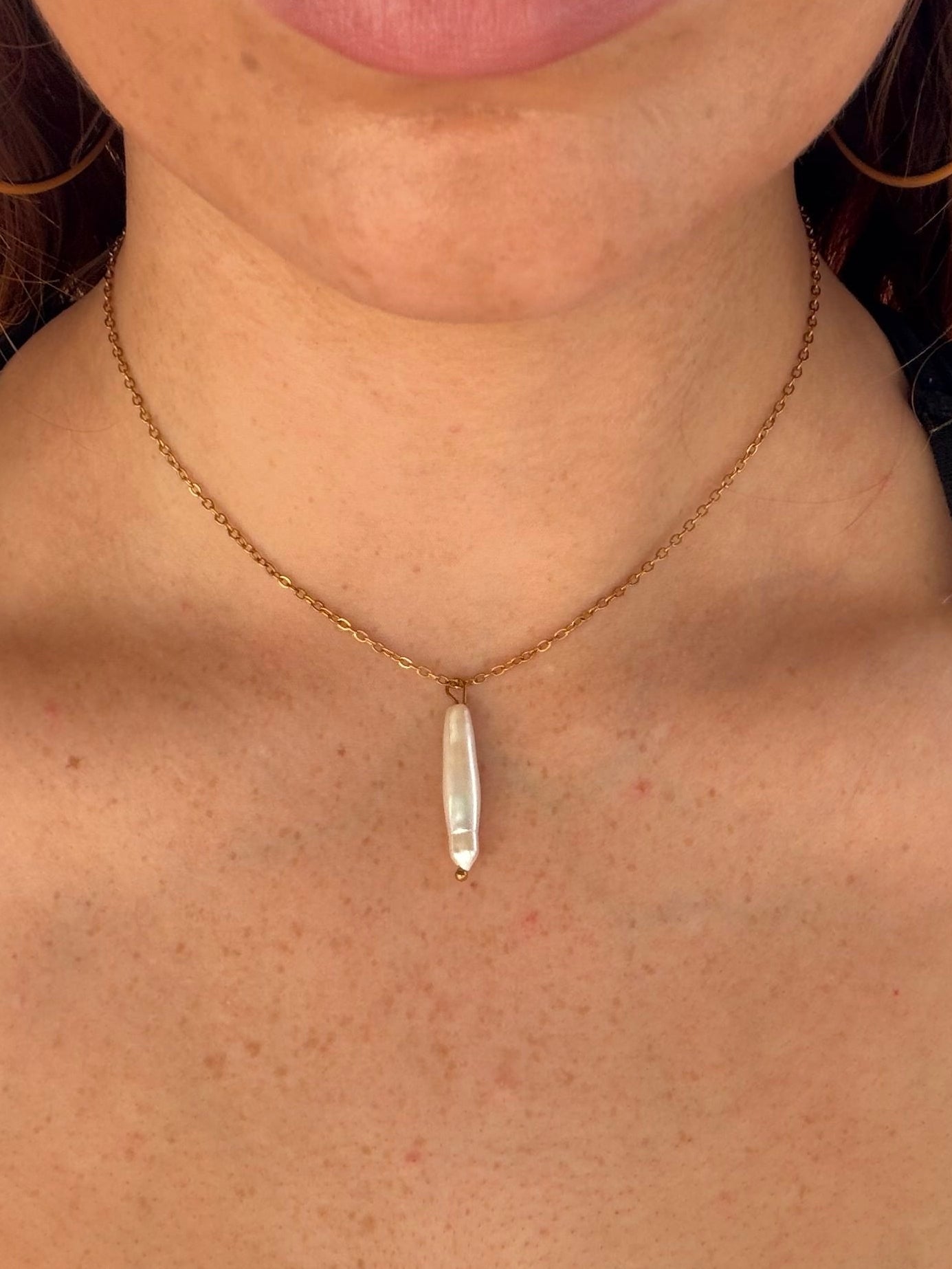 Close-up of a person wearing a gold necklace with a pearl pendant.