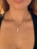Close-up of a person wearing a necklace with a pearl long narrow pendant.