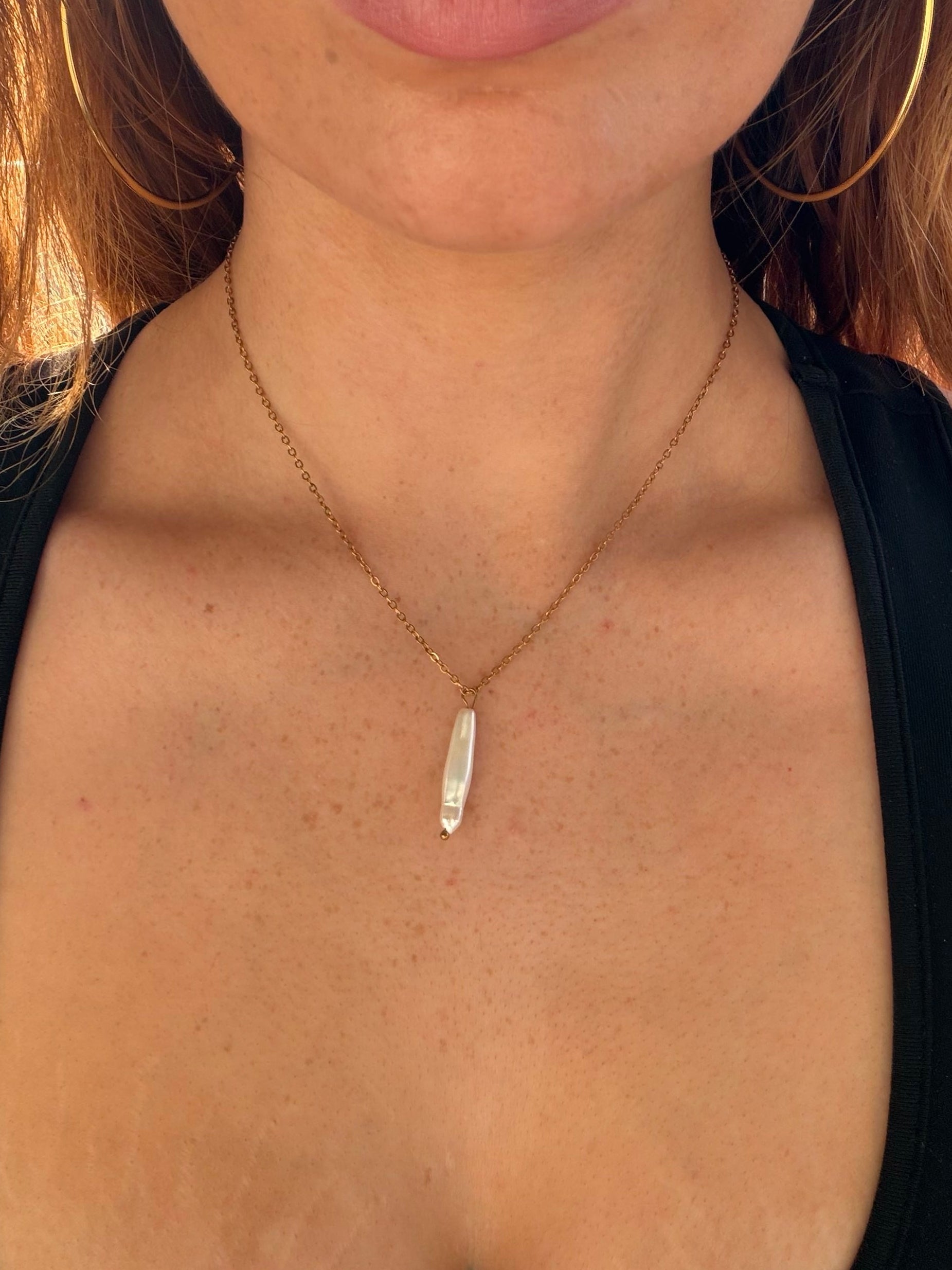 Close-up of a person wearing a necklace with a pearl long narrow pendant.